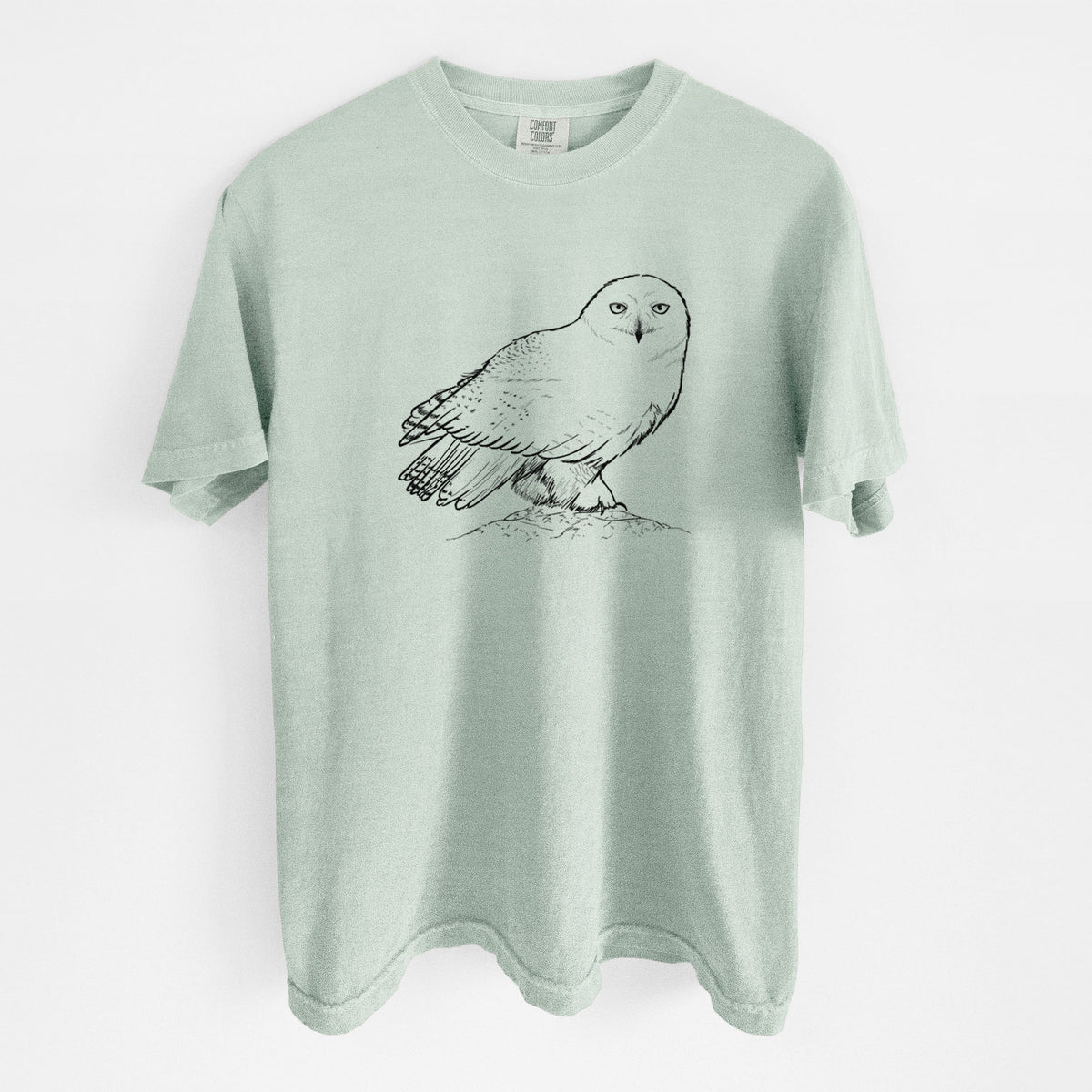 Bay green Comfort Colors t-shirt laid flat, printed with a detailed black ink illustration of a snowy owl perched on a snowy mound.