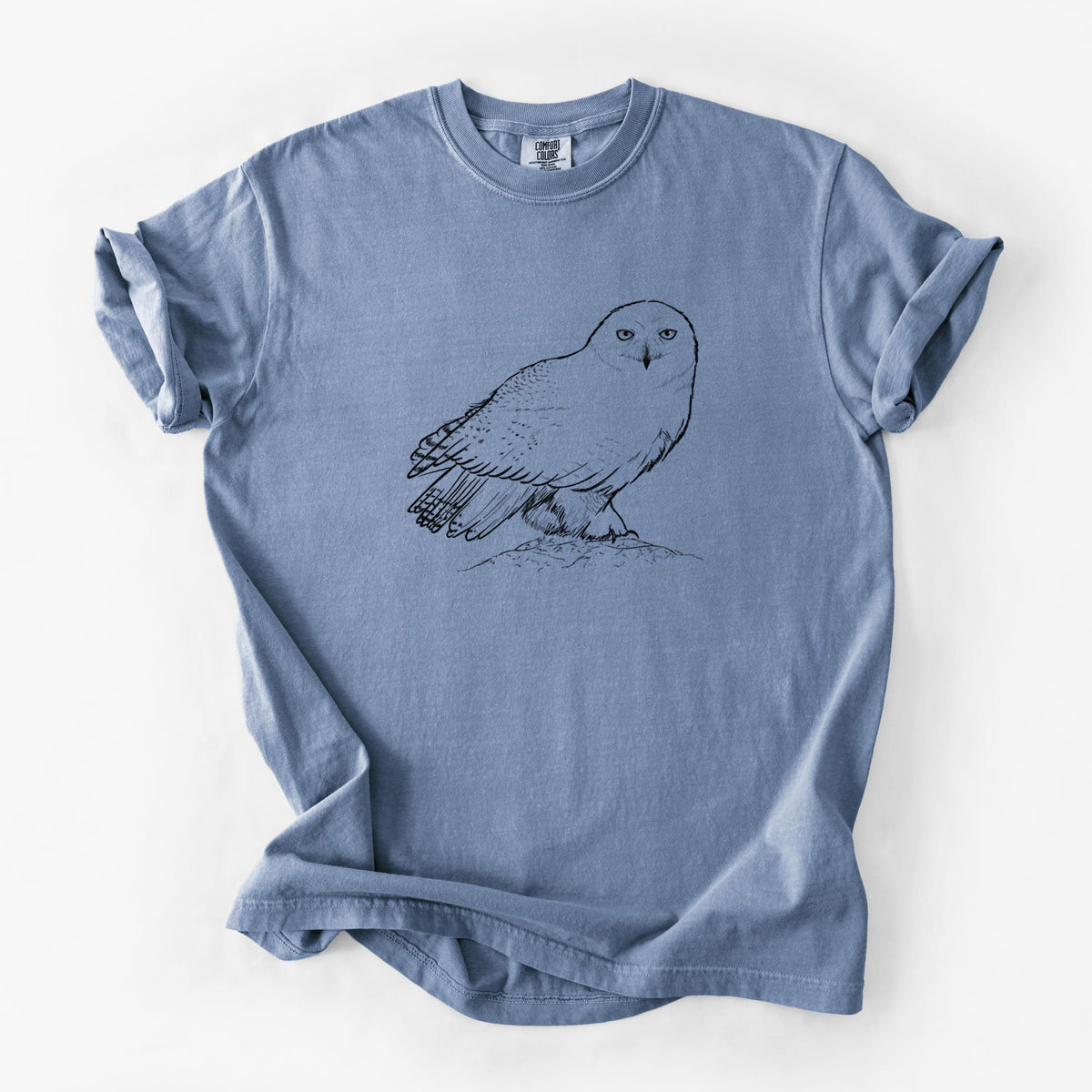 Blue jean Comfort Colors t-shirt laid flat, printed with a detailed black ink illustration of a snowy owl perched on a snowy mound.