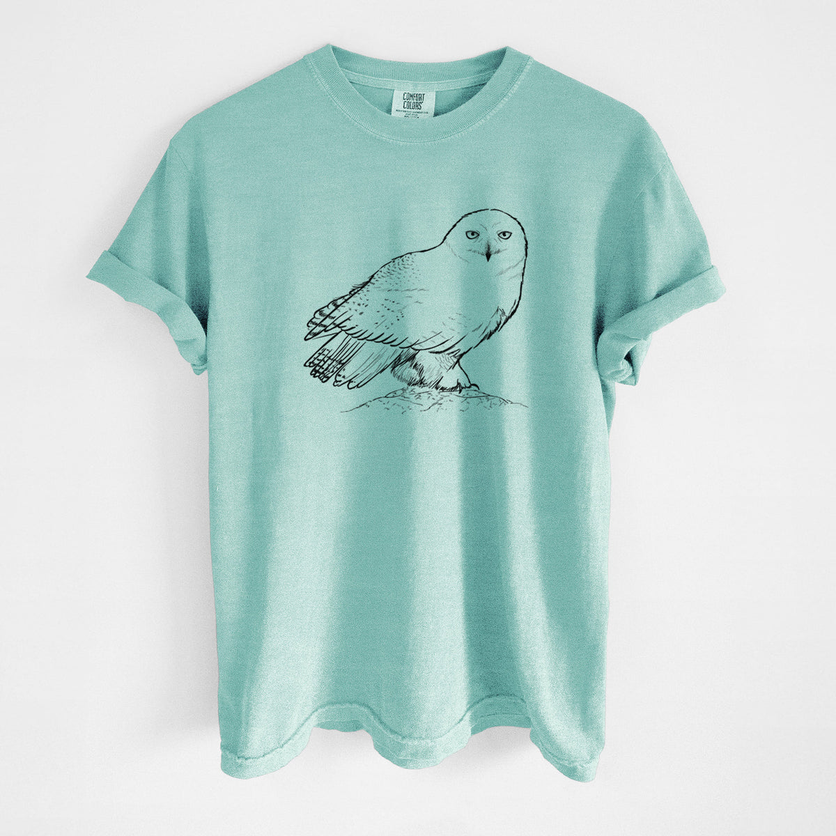 Chalky mint Comfort Colors t-shirt laid flat, printed with a detailed black ink illustration of a snowy owl perched on a snowy mound.