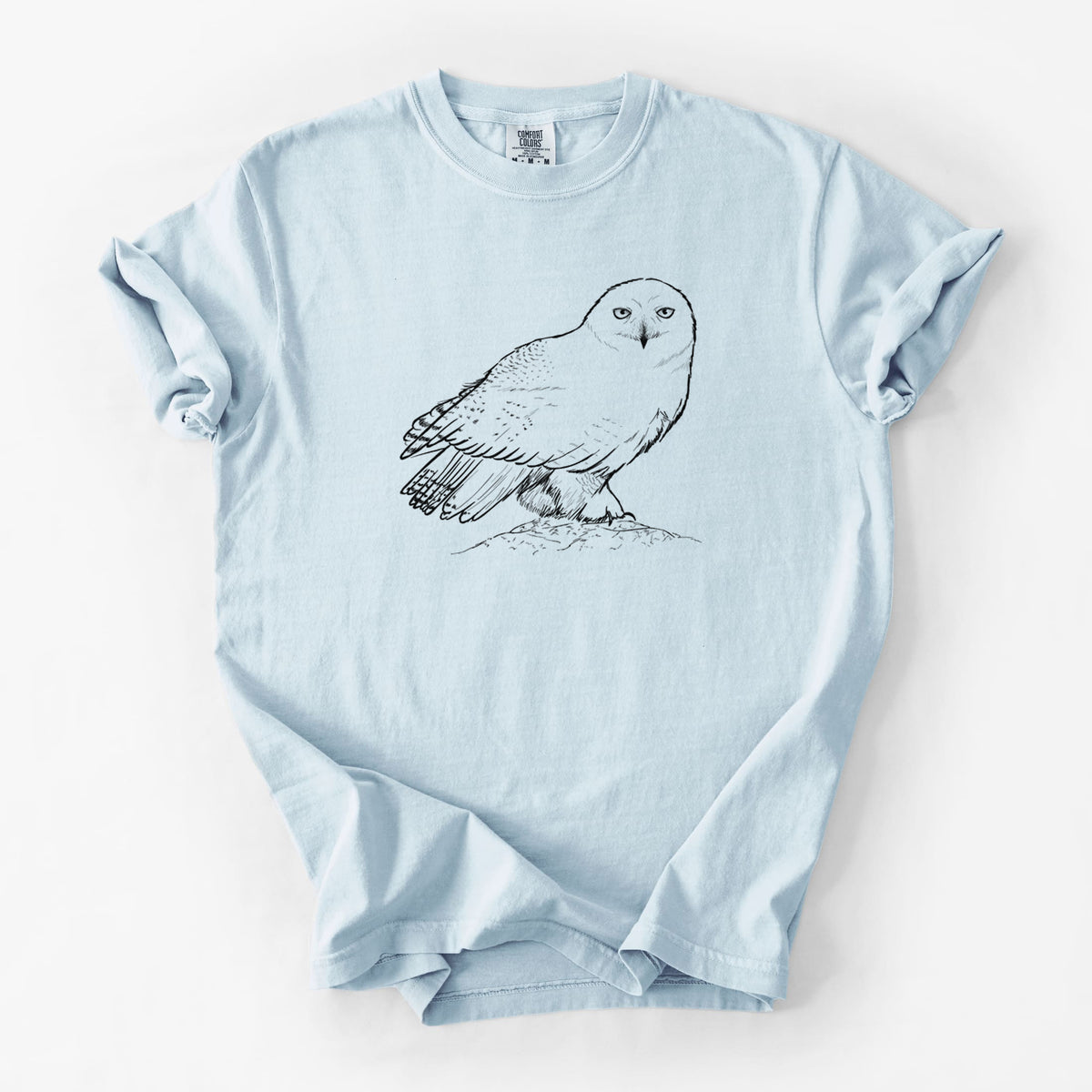 Chambray blue Comfort Colors t-shirt laid flat, printed with a detailed black ink illustration of a snowy owl perched on a snowy mound.