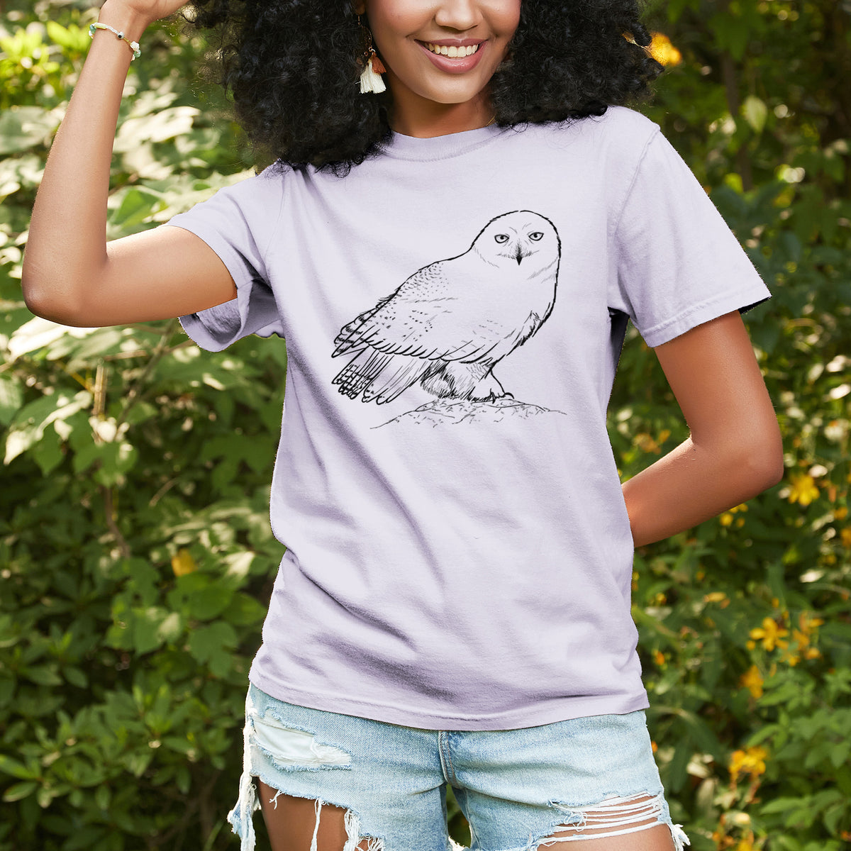 Woman wearing a Comfort Colors t-shirt printed with a detailed black ink illustration of a snowy owl perched on a snowy mound, outdoors.