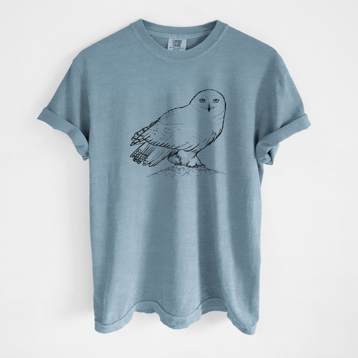 Steel blue Comfort Colors t-shirt laid flat, printed with a detailed black ink illustration of a snowy owl perched on a snowy mound.