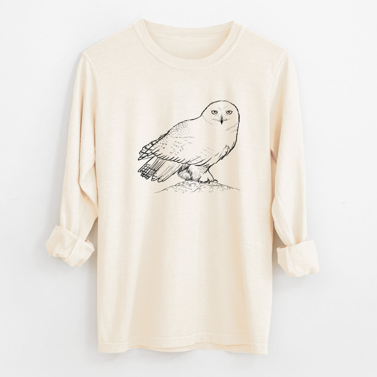 Ivory Comfort Colors long sleeve shirt laid flat with the cuffs rolled, printed with a detailed black ink illustration of a snowy owl perched on a snowy mound.