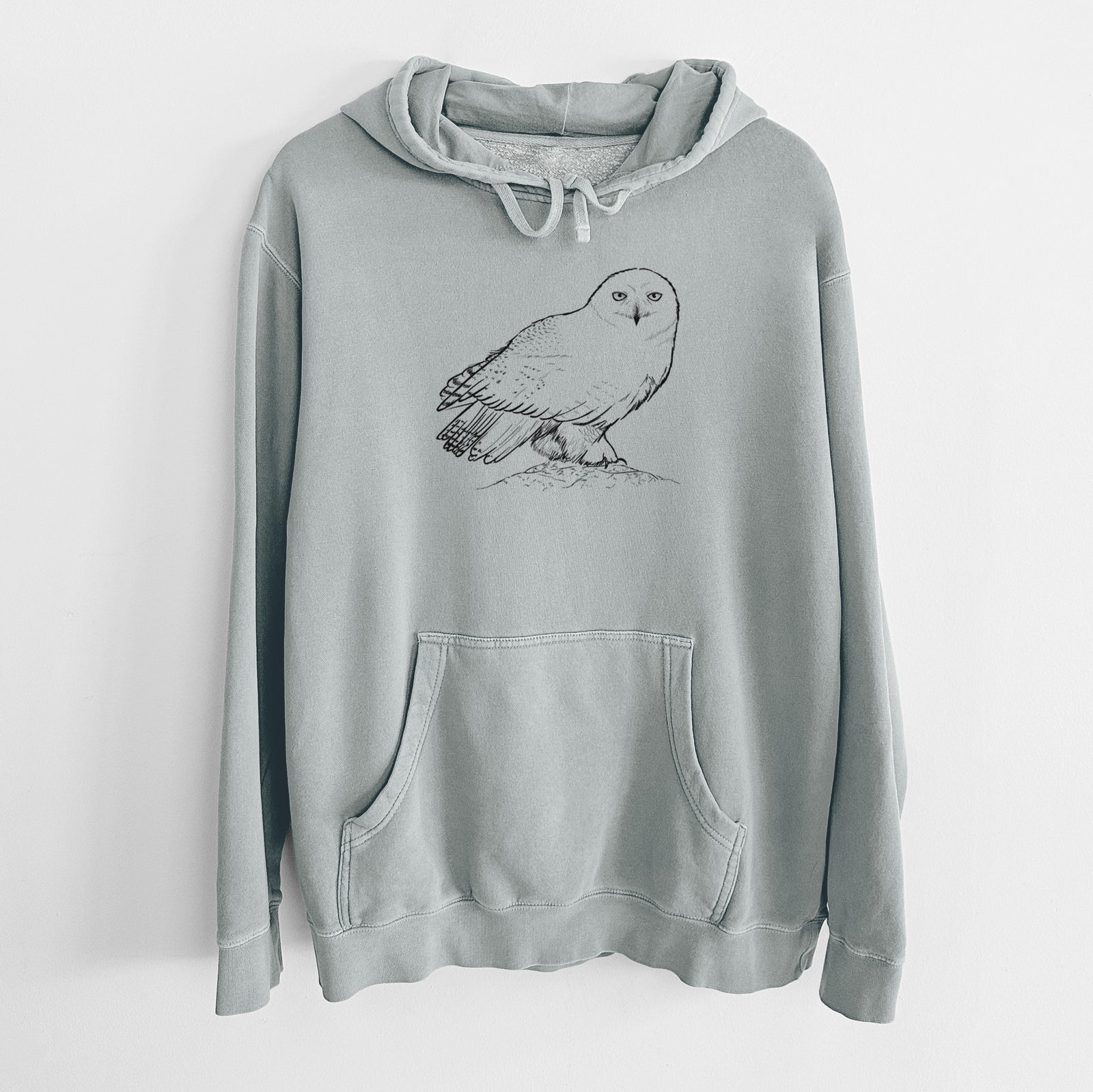 Sage green pigment dyed hoodie laid flat, printed with a detailed black ink illustration of a snowy owl perched on a snowy mound.