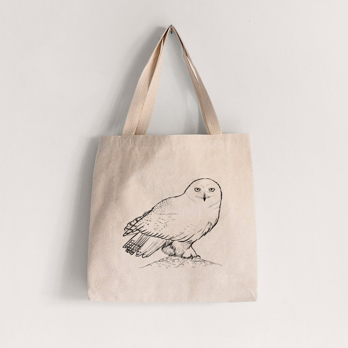 Natural canvas tote bag printed with a detailed black ink illustration of a snowy owl perched on a snowy mound.