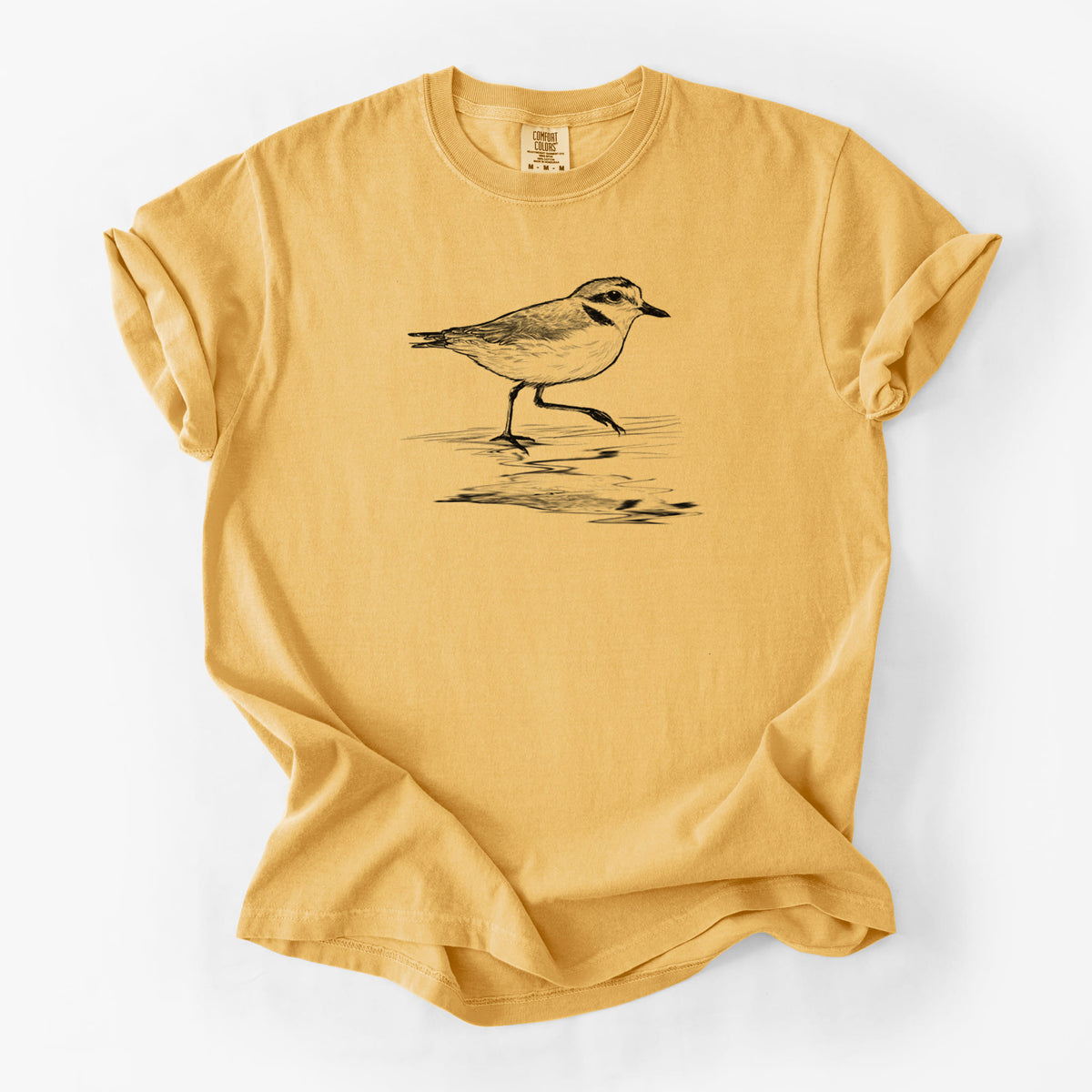 Golden wheat yellow Comfort Colors t-shirt laid flat, printed with a black ink sketch of a snowy plover running along the wet shoreline.