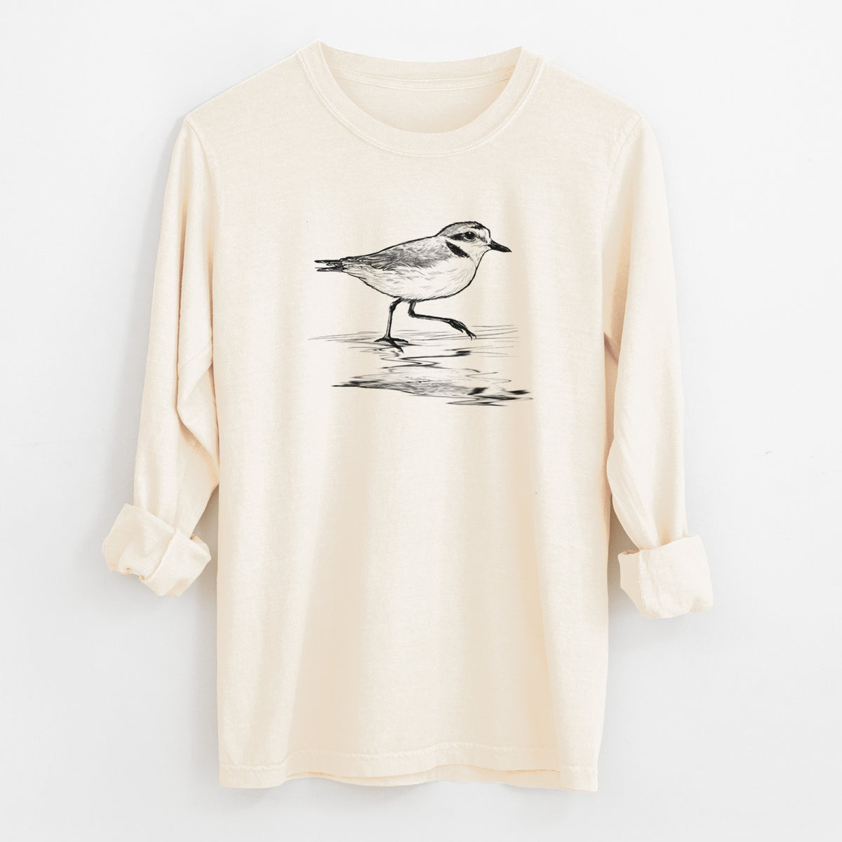Ivory Comfort Colors long sleeve shirt laid flat with the cuffs rolled, printed with a black ink sketch of a snowy plover running along the wet shoreline.