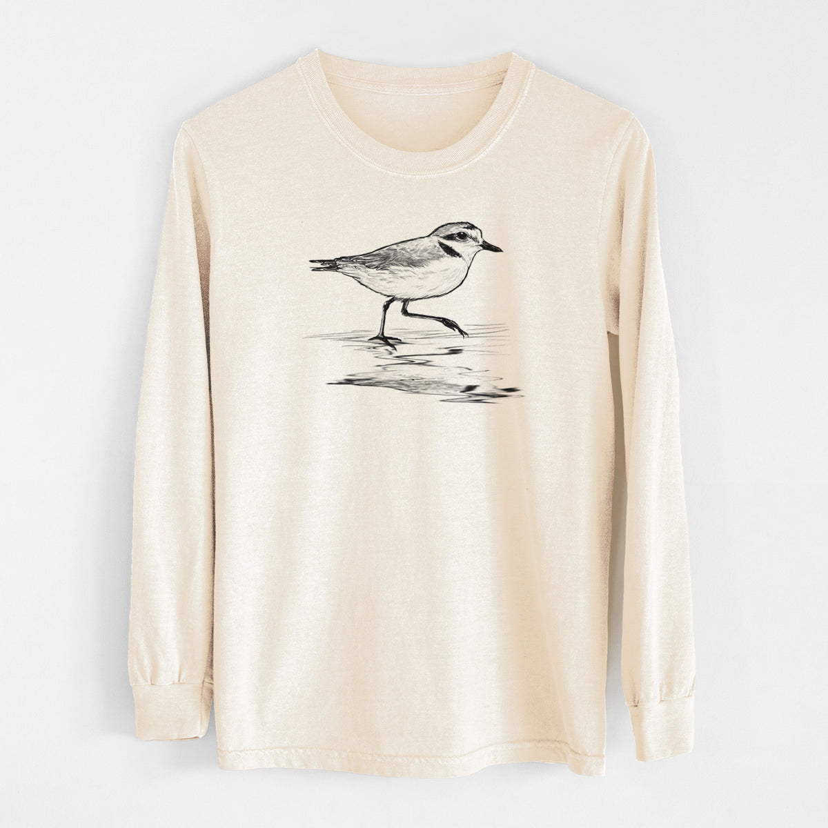 Ivory Comfort Colors long sleeve shirt laid flat, printed with a black ink sketch of a snowy plover running along the wet shoreline.