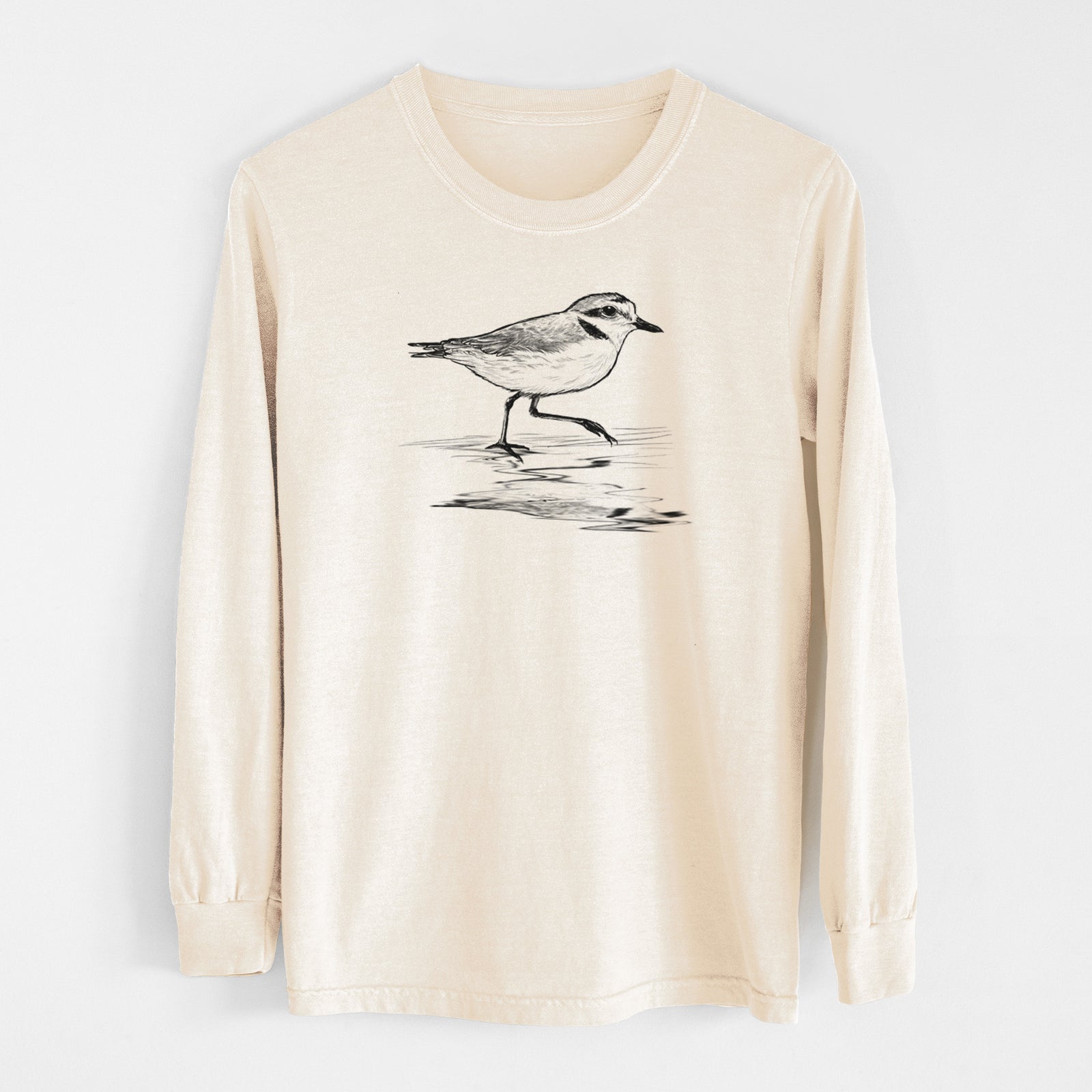 Ivory Comfort Colors long sleeve shirt laid flat, printed with a black ink sketch of a snowy plover running along the wet shoreline.