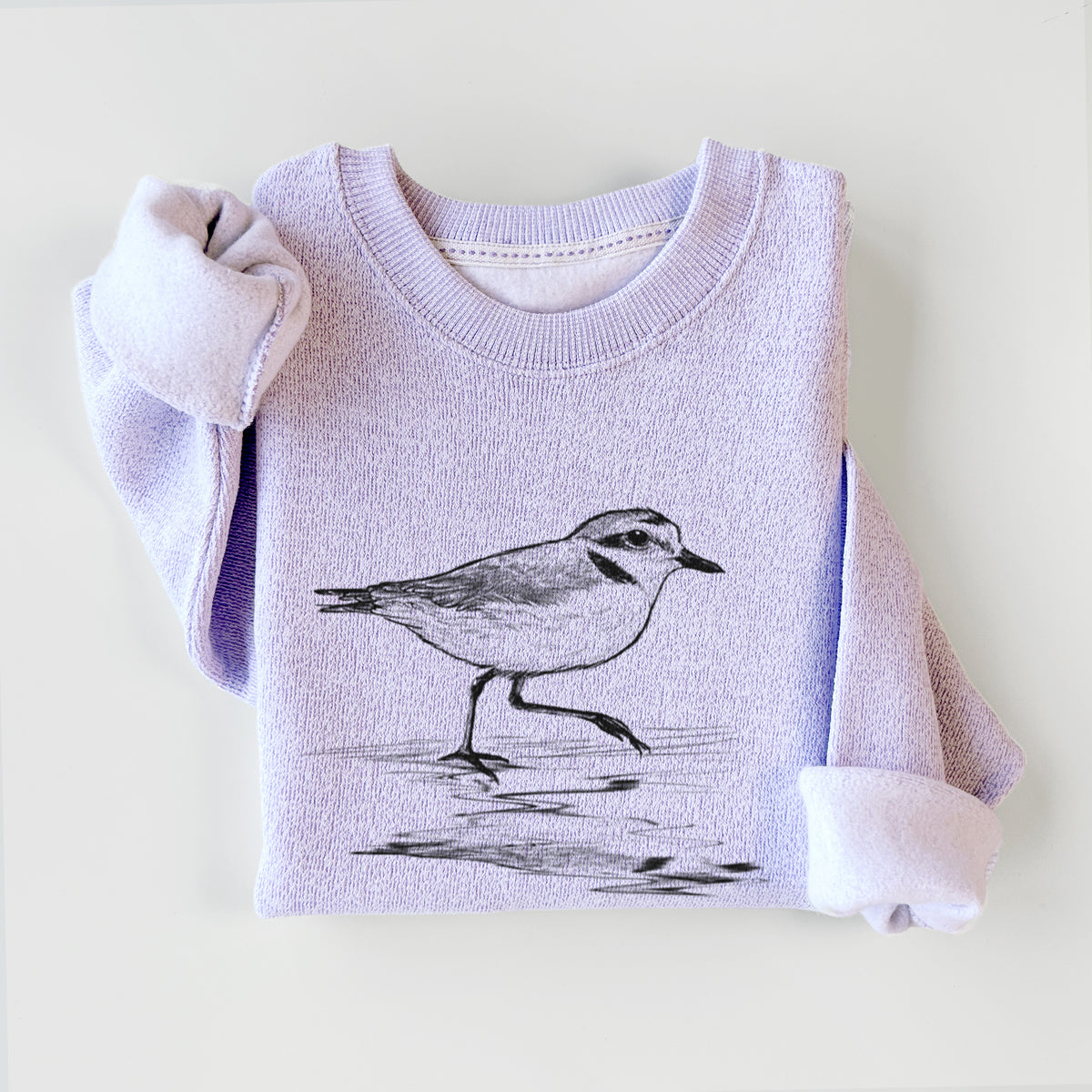 Ice purple knit sweatshirt printed with a black ink sketch of a snowy plover running along the wet shoreline, styled flat.