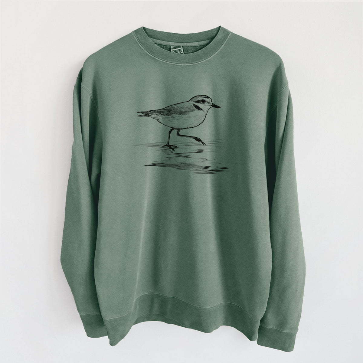Alpine green pigment dyed crewneck sweatshirt laid flat, printed with a black ink sketch of a snowy plover running along the wet shoreline.