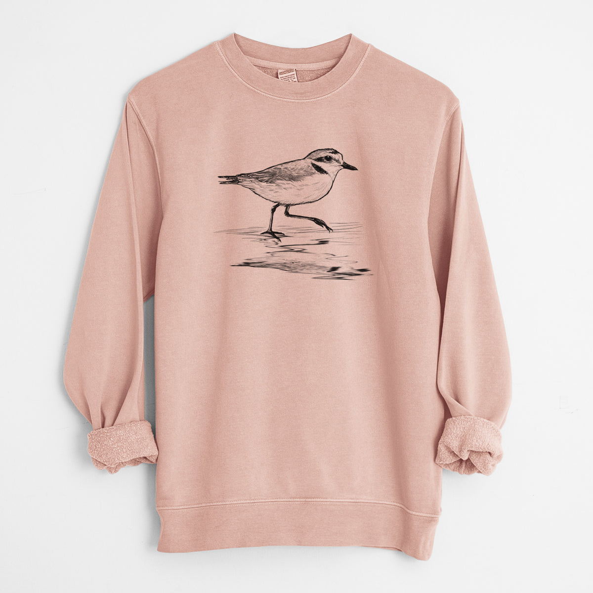 Dusty pink pigment dyed crewneck sweatshirt laid flat with the sleeves rolled, printed with a black ink sketch of a snowy plover running along the wet shoreline.