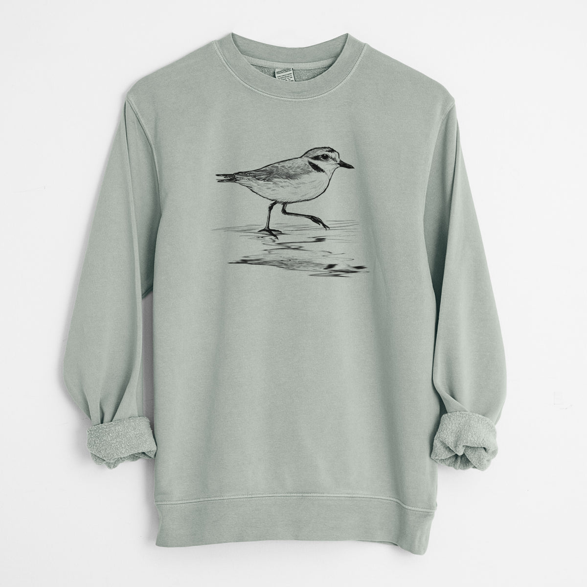 Sage green pigment dyed crewneck sweatshirt laid flat with the sleeves rolled, printed with a black ink sketch of a snowy plover running along the wet shoreline.
