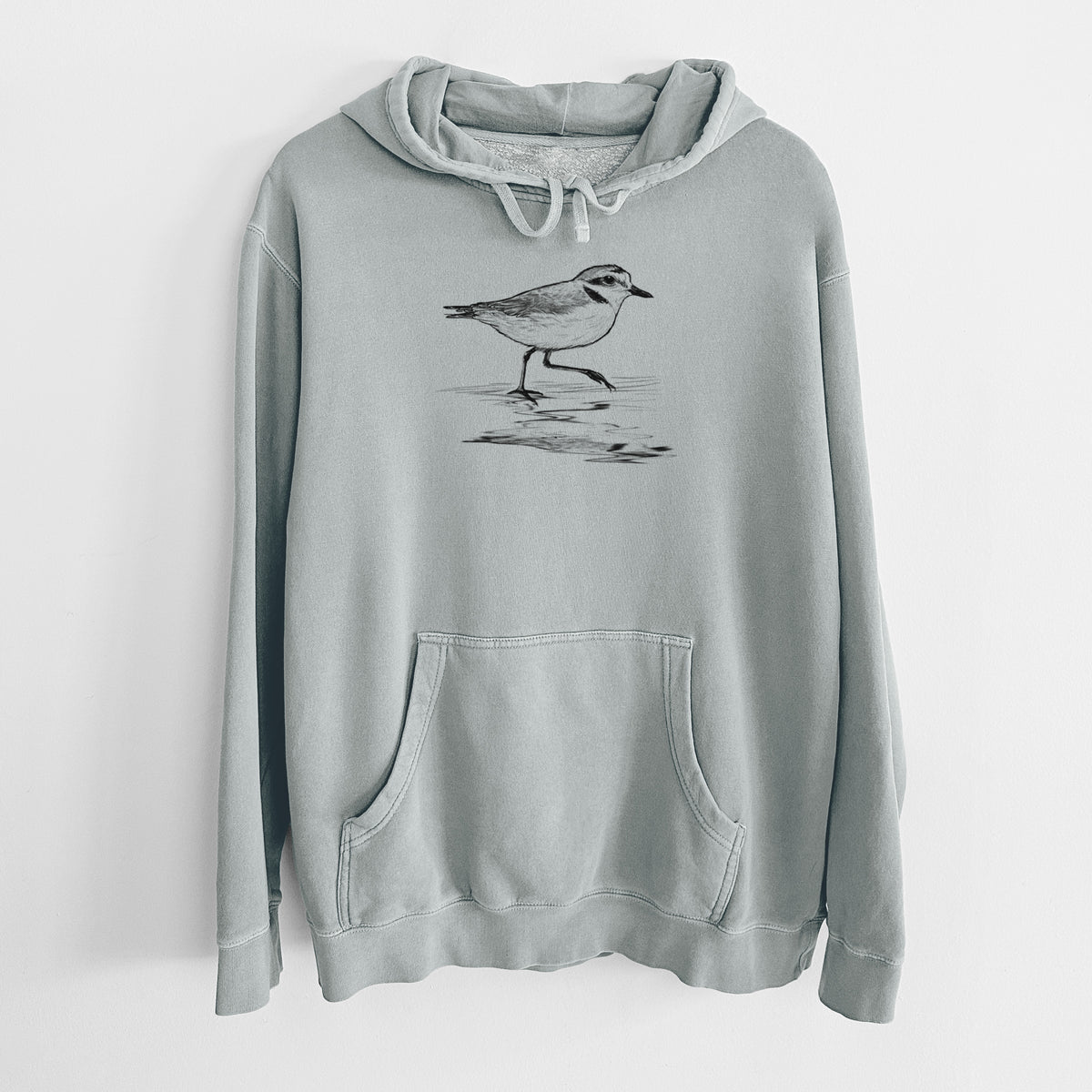 Sage green pigment dyed hoodie laid flat, printed with a black ink sketch of a snowy plover running along the wet shoreline.