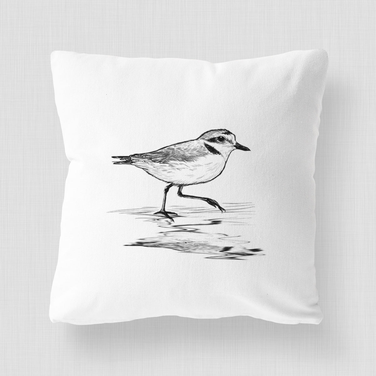 White pillow cover printed with a black ink sketch of a snowy plover running along the wet shoreline.