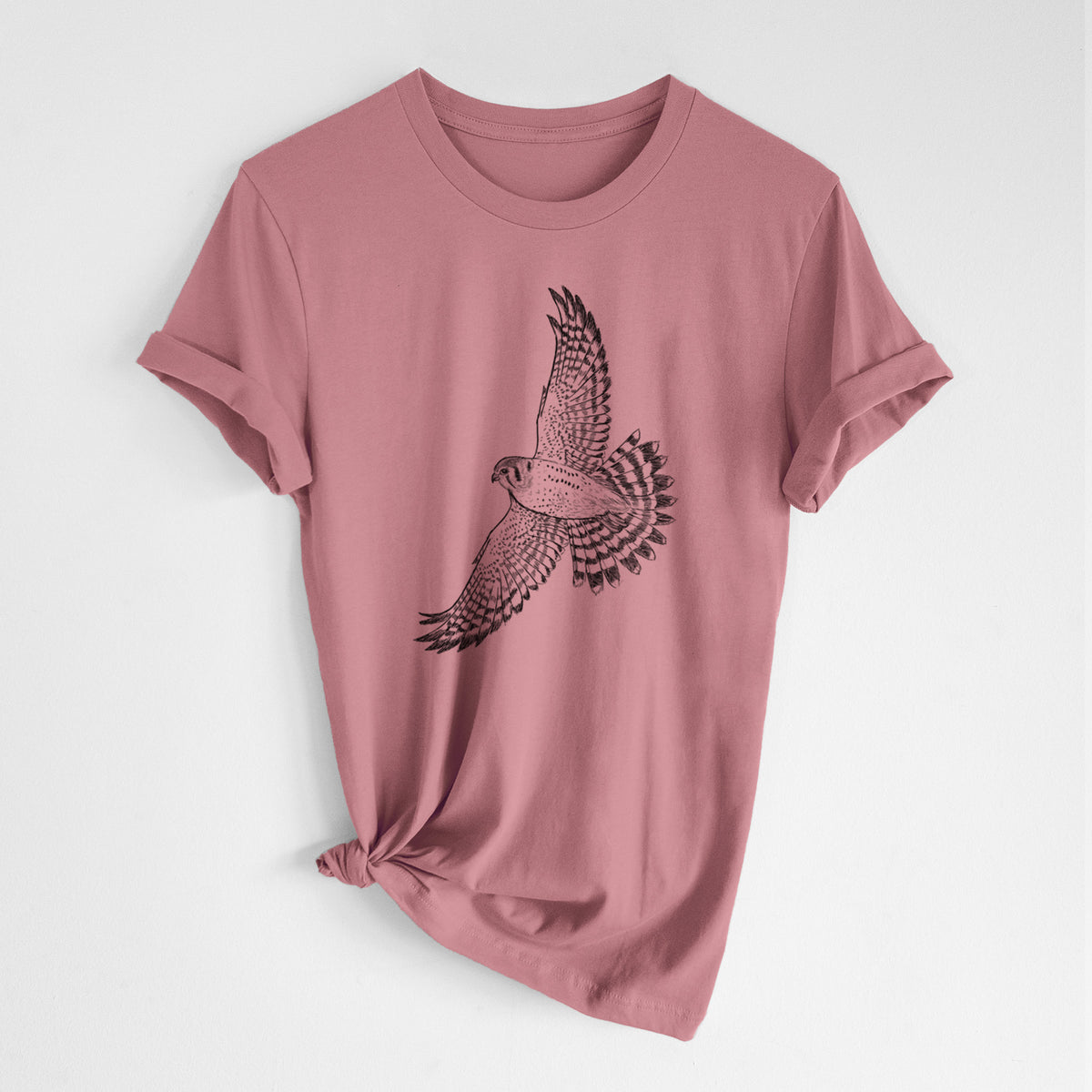 Mauve pink lightweight cotton t-shirt laid flat with the sleeves rolled, printed with a detailed black ink illustration of an American kestrel in flight with its wings raised.