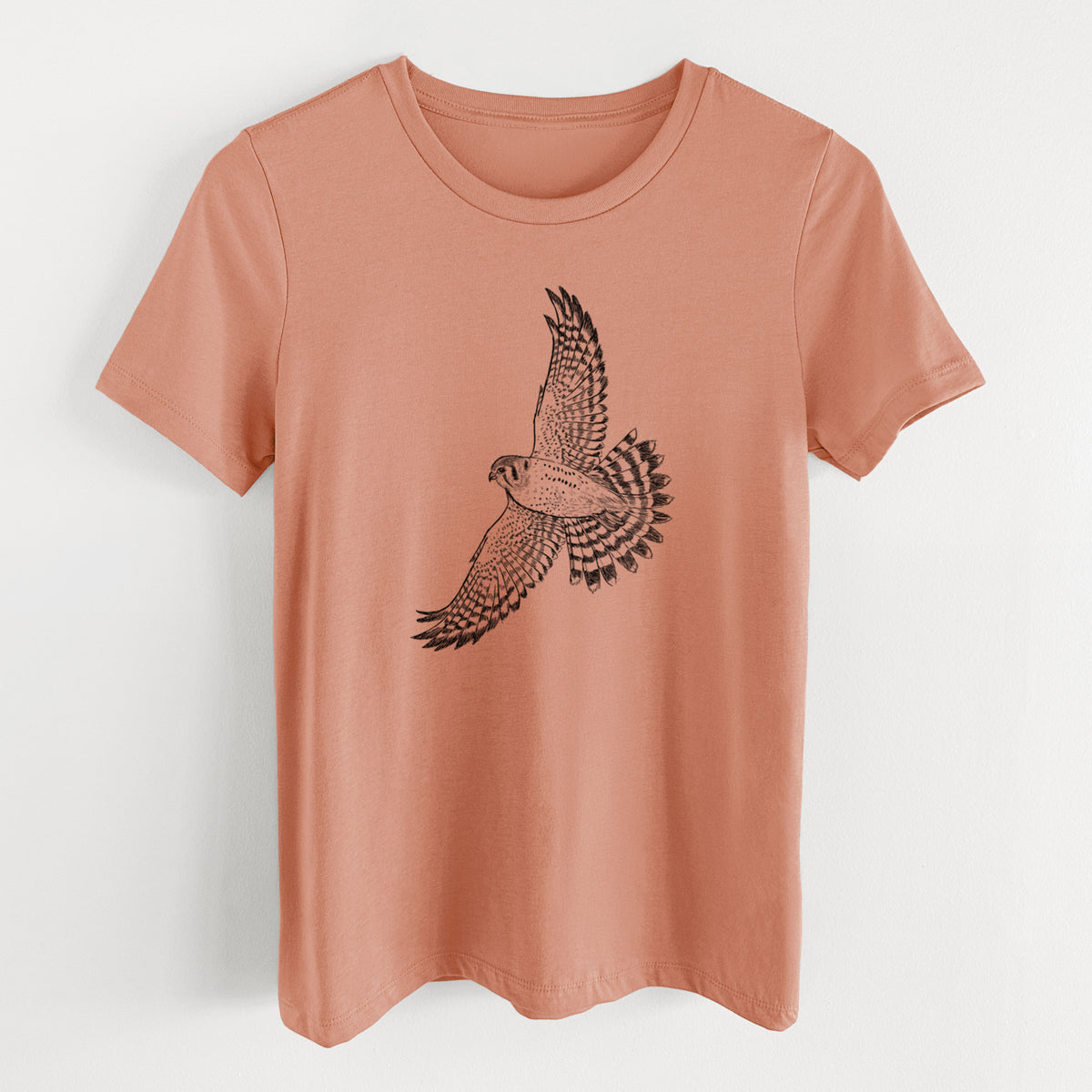 Terracotta orange women's relaxed fit cotton t-shirt laid flat, printed with a detailed black ink illustration of an American kestrel in flight with its wings raised.