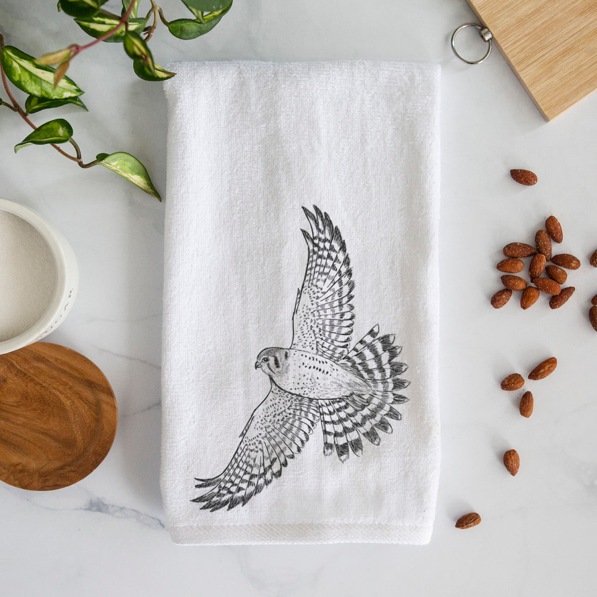 White hand towel printed with a detailed black ink illustration of an American kestrel in flight with its wings raised.