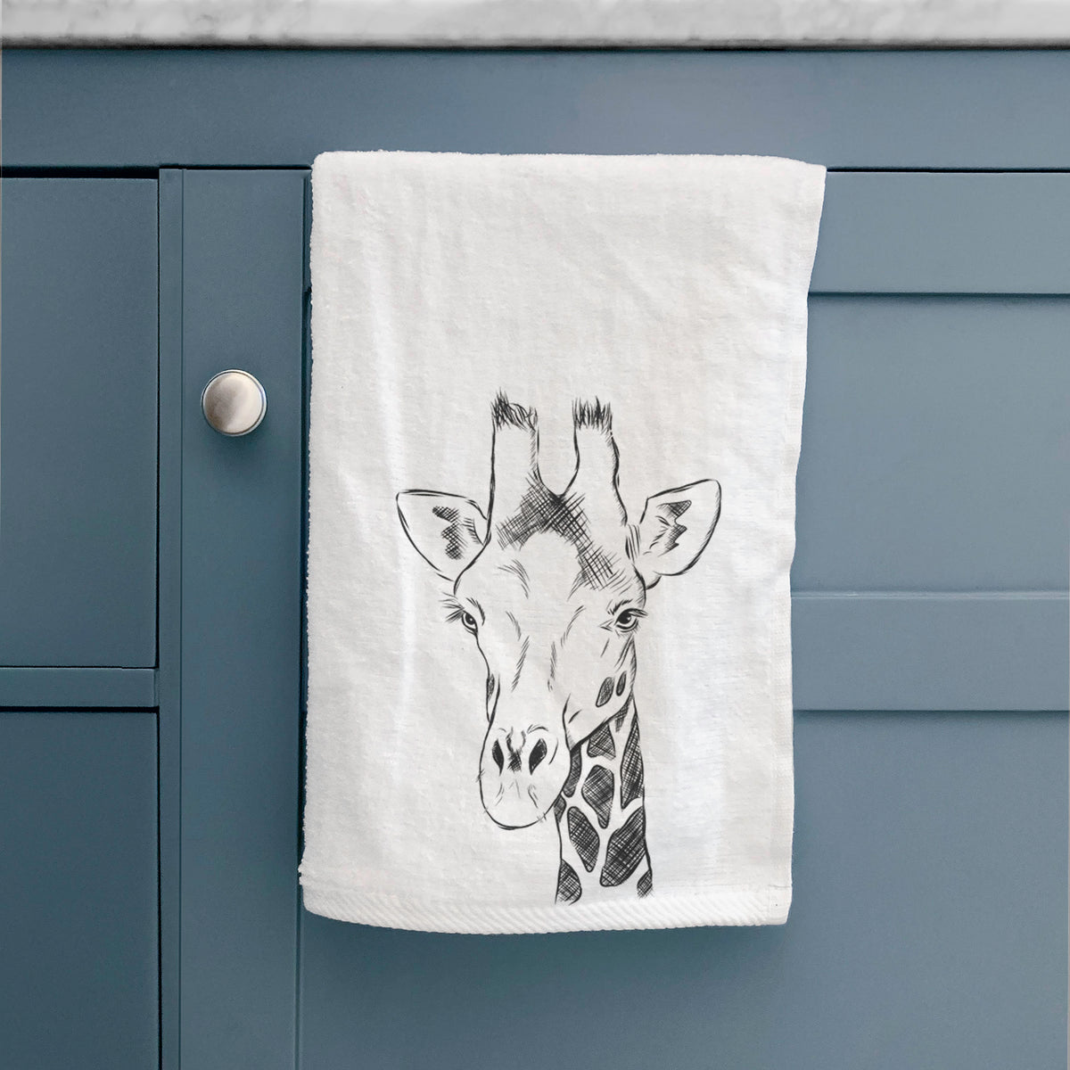 White hand towel printed with a black ink portrait of a southern giraffe's head and neck, hanging on a cabinet door.