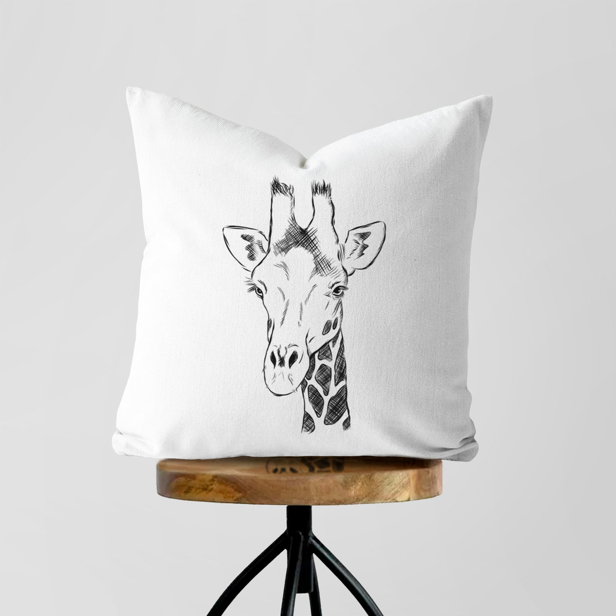 White pillow cover printed with a black ink portrait of a southern giraffe's head and neck, on a wooden stool.