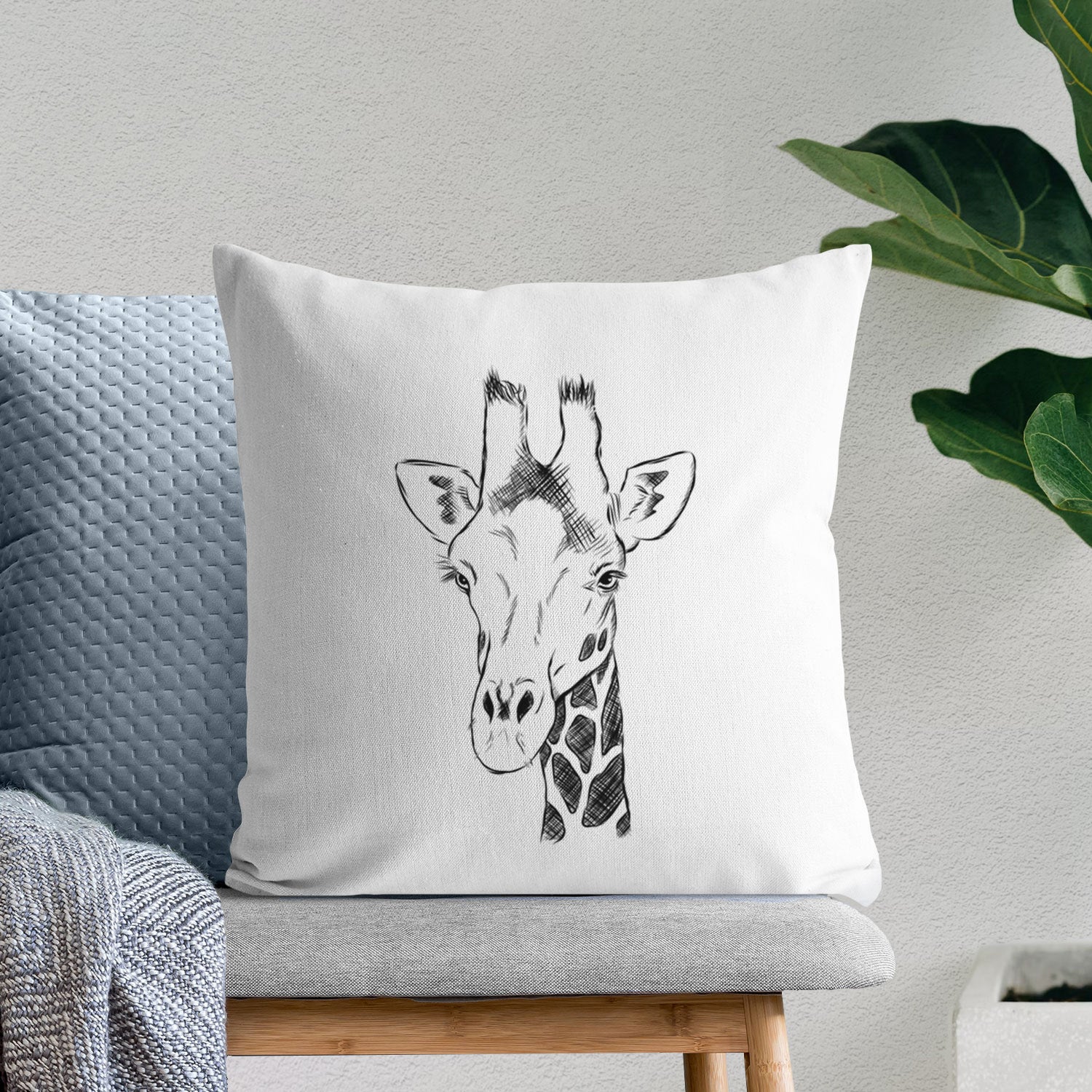 White pillow cover printed with a black ink portrait of a southern giraffe's head and neck, on a bench beside plants.