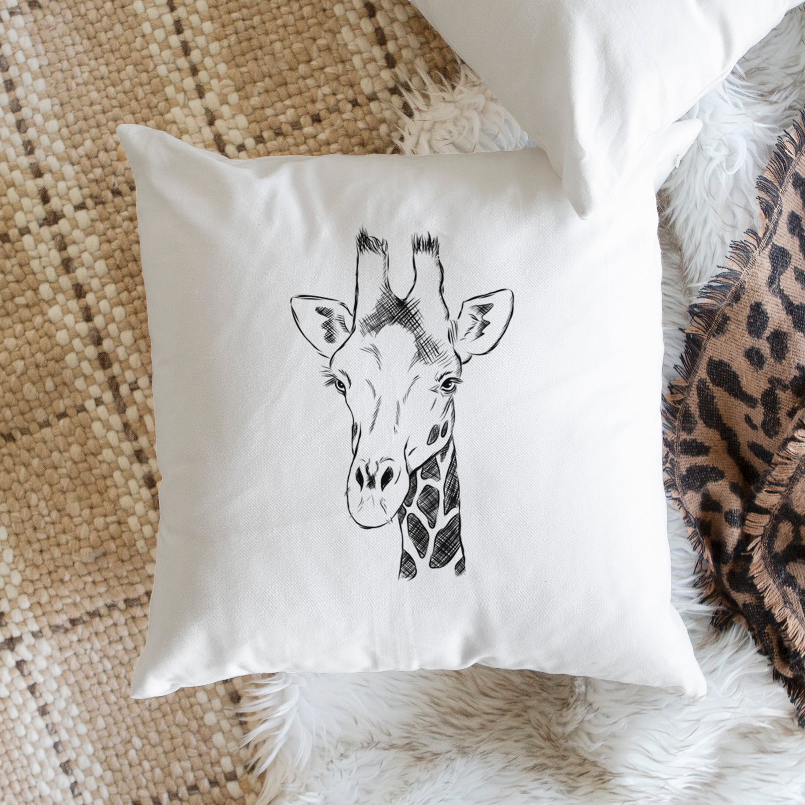 White pillow cover printed with a black ink portrait of a southern giraffe's head and neck, on a bench beside plants.
