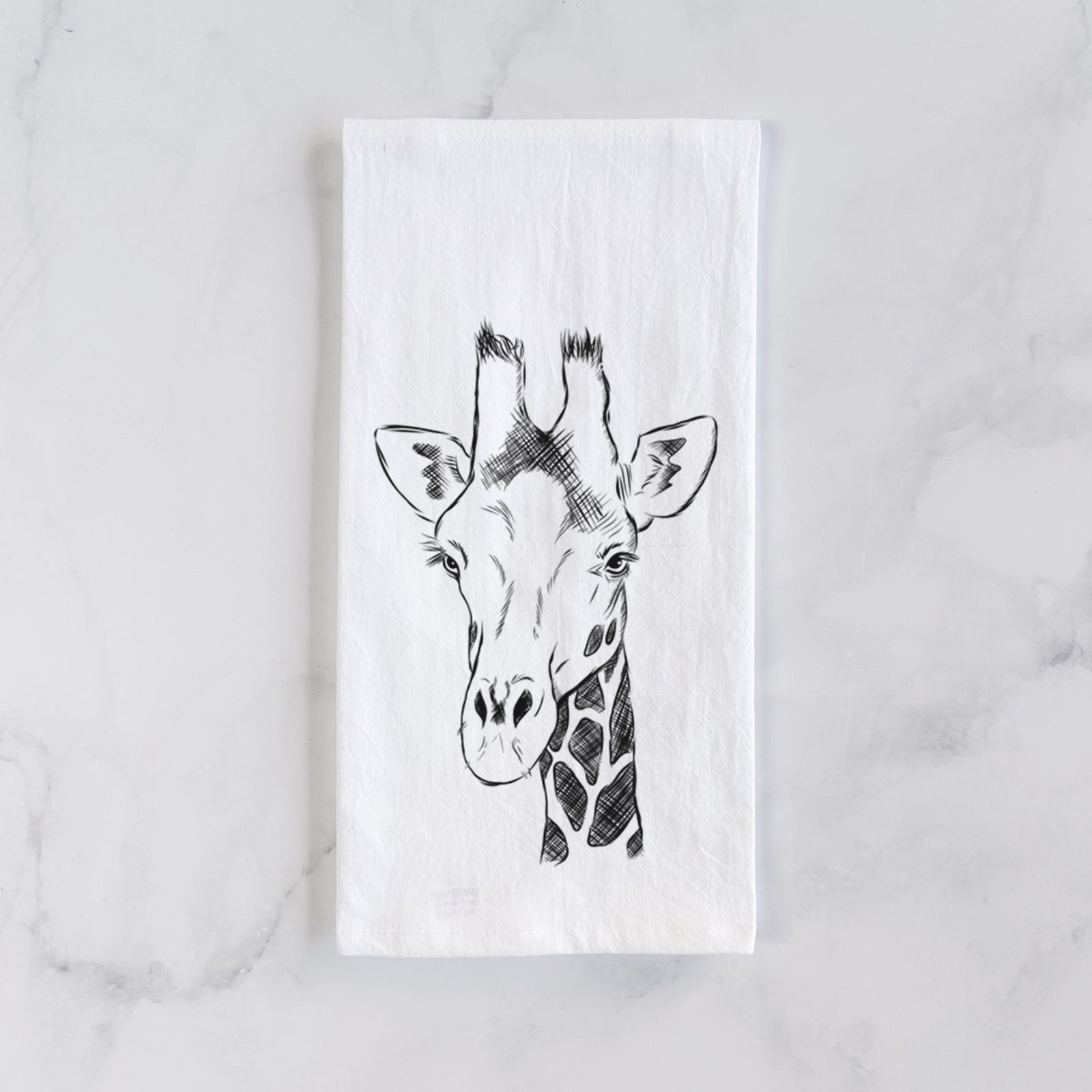 White cotton tea towel printed with a black ink portrait of a southern giraffe's head and neck, on a marble counter beside a round wooden cutting board and greenery.
