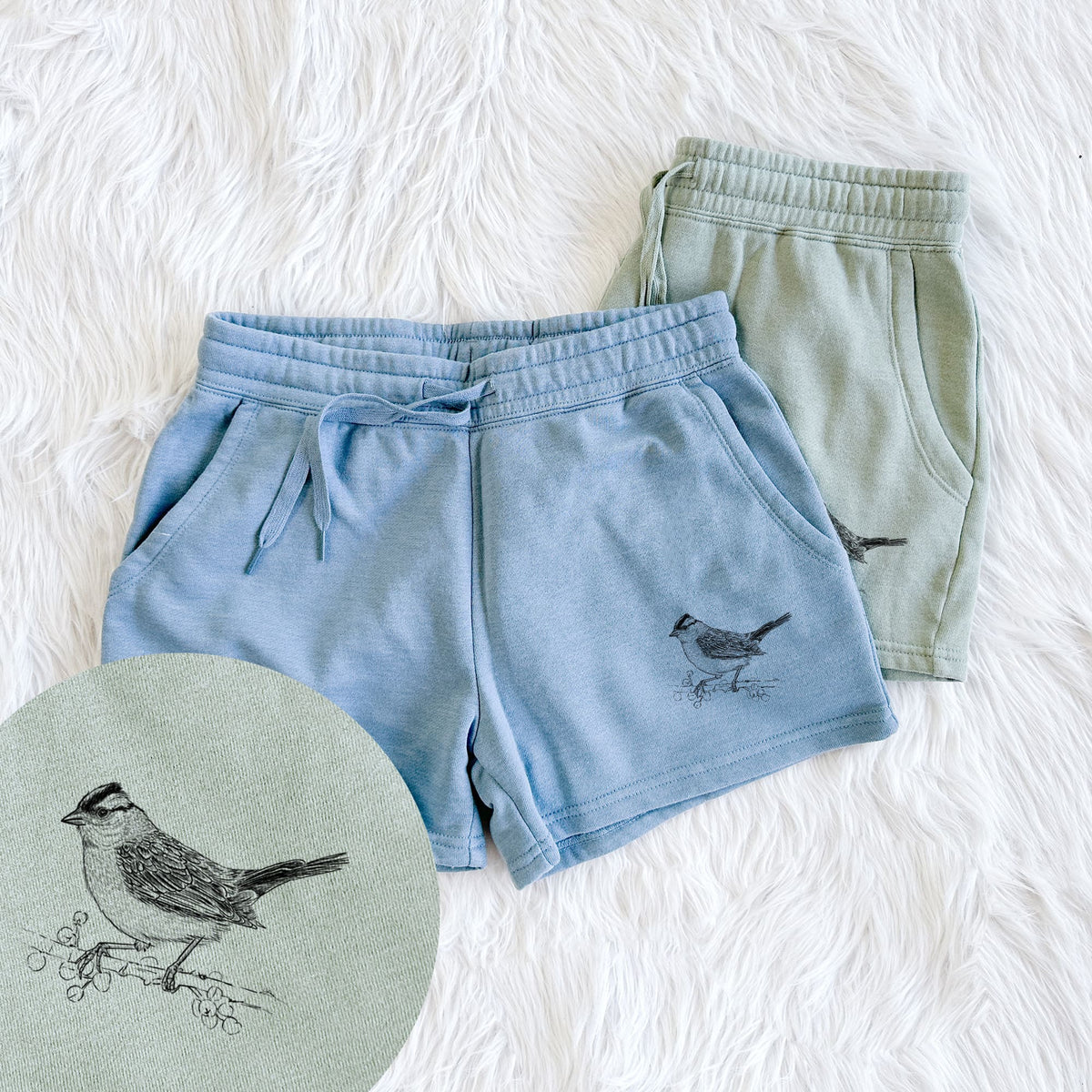 Two pairs of Cali Wave shorts in different colors printed with a detailed black ink sketch of a white-crowned sparrow perched on a branch, with a close-up of the print.