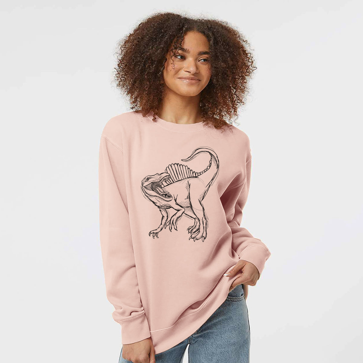 Model wearing a dusty pink pigment dyed crewneck sweatshirt printed with a black ink illustration of a Spinosaurus with its tall sail-shaped back.