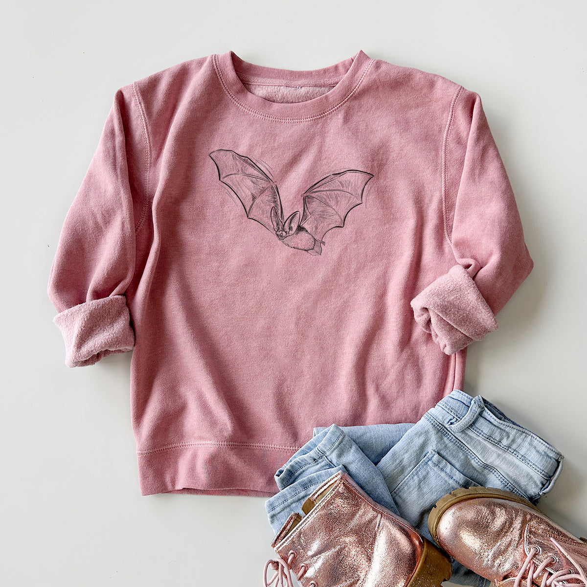 Youth crewneck sweatshirt printed with a black ink illustration of a spotted bat in flight with large ears, styled flat with jeans and boots.