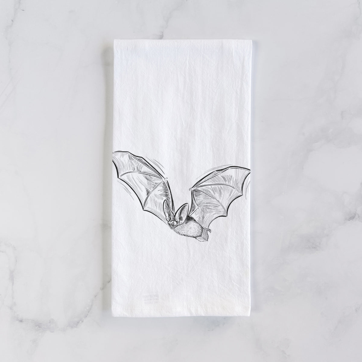 White cotton tea towel laid flat on marble, printed with a black ink illustration of a spotted bat in flight with large ears.