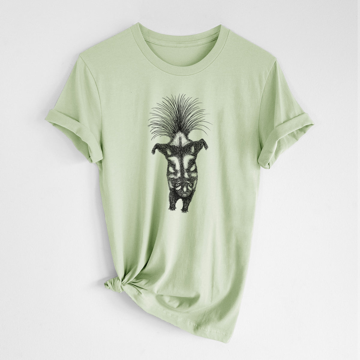 Spring green lightweight cotton t-shirt laid flat with the sleeves rolled, printed with a black ink illustration of a spotted skunk doing a handstand with its tail fanned.