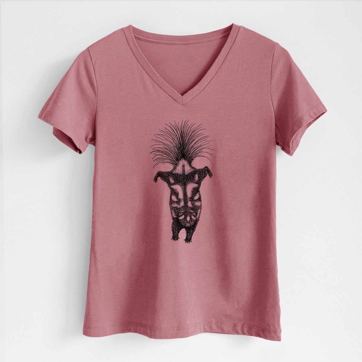 Mauve pink women's relaxed fit cotton V-neck t-shirt laid flat, printed with a black ink illustration of a spotted skunk doing a handstand with its tail fanned.