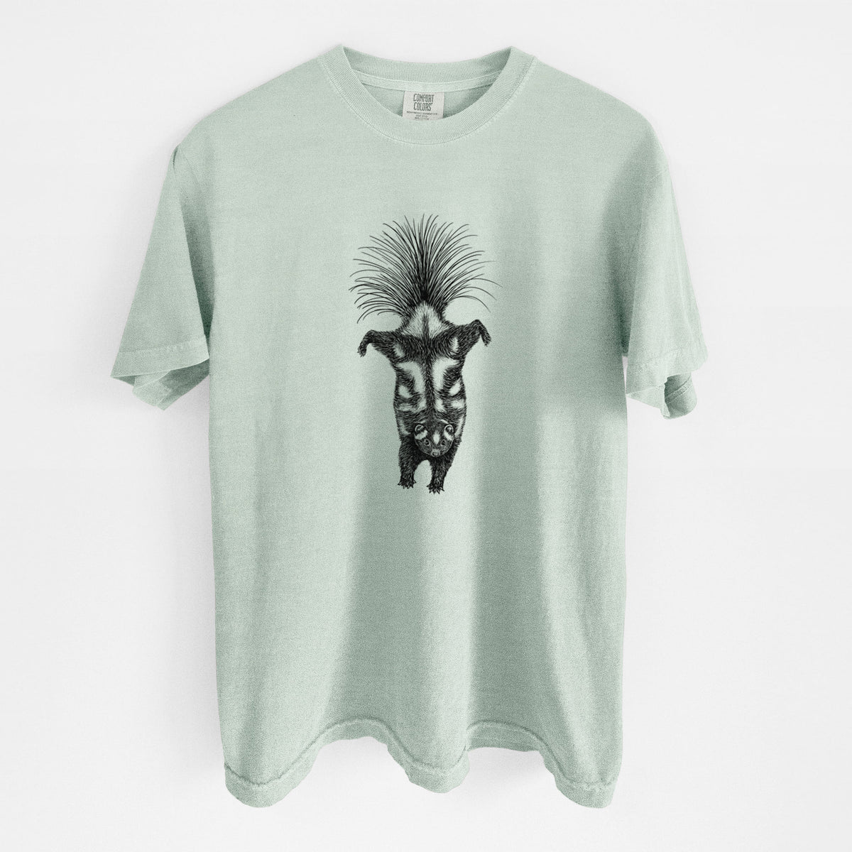 Bay green Comfort Colors t-shirt laid flat, printed with a black ink illustration of a spotted skunk doing a handstand with its tail fanned.