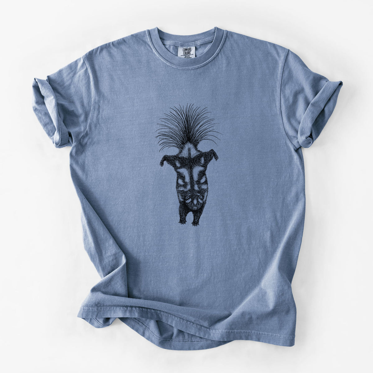 Blue jean Comfort Colors t-shirt laid flat, printed with a black ink illustration of a spotted skunk doing a handstand with its tail fanned.