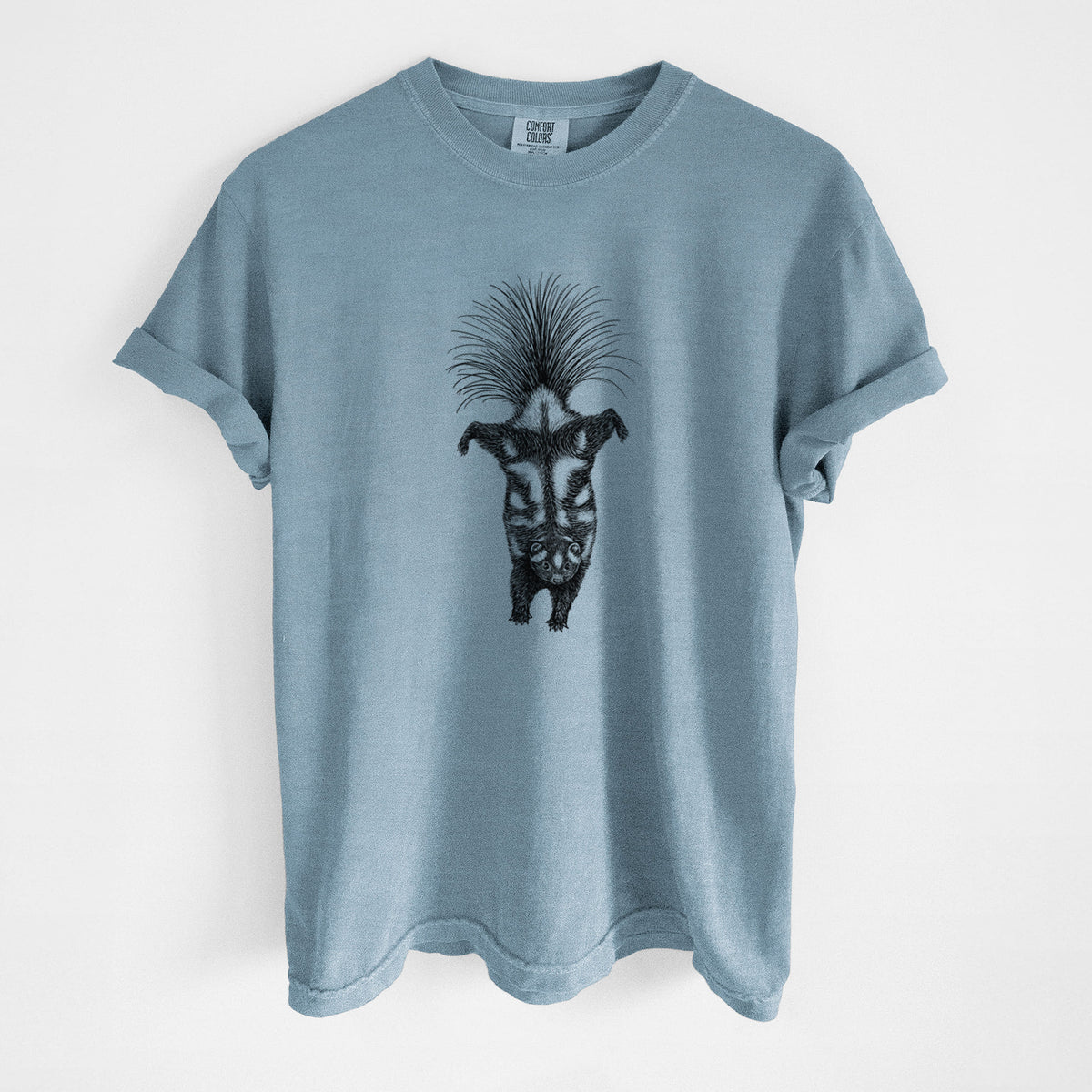 Steel blue Comfort Colors t-shirt laid flat, printed with a black ink illustration of a spotted skunk doing a handstand with its tail fanned.