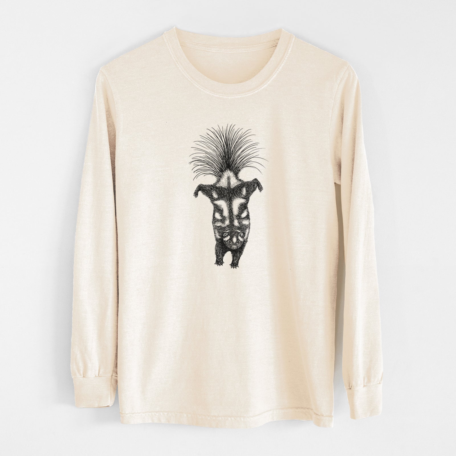 Ivory Comfort Colors long sleeve shirt laid flat, printed with a black ink illustration of a spotted skunk doing a handstand with its tail fanned.