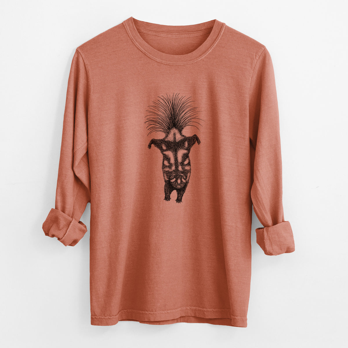 Yam burnt orange Comfort Colors long sleeve shirt laid flat with the cuffs rolled, printed with a black ink illustration of a spotted skunk doing a handstand with its tail fanned.