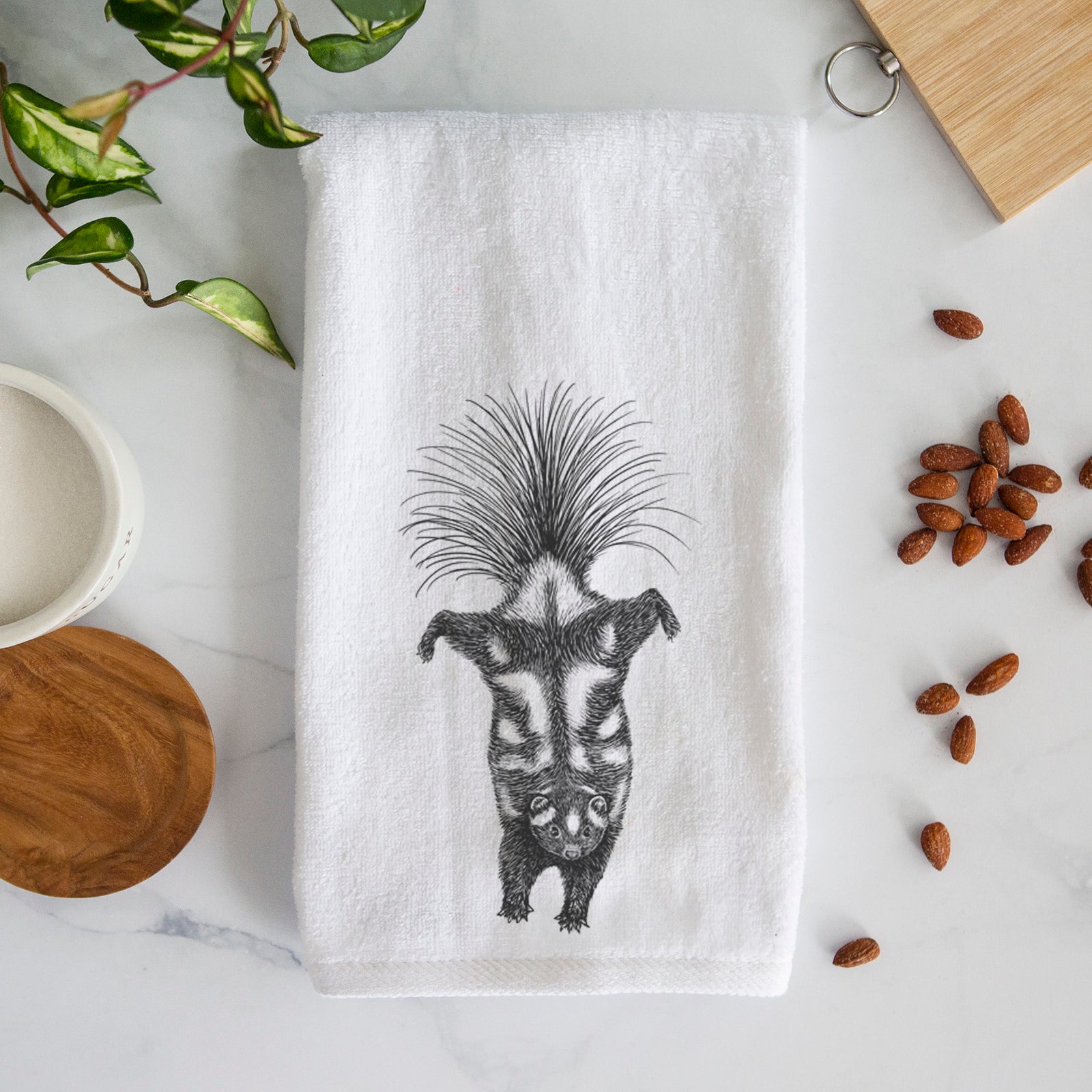 White hand towel printed with a black ink illustration of a spotted skunk doing a handstand with its tail fanned.