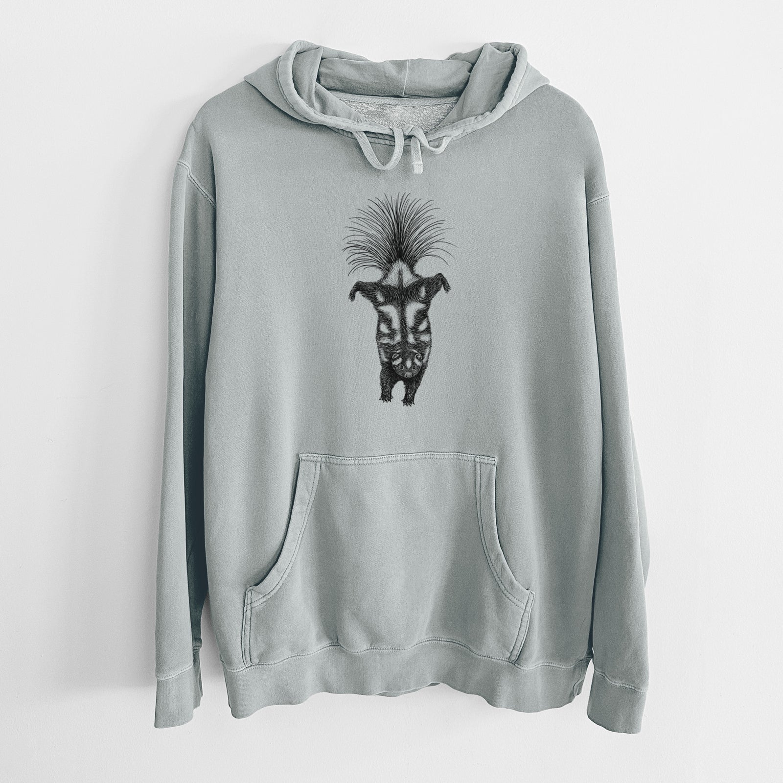 Sage green pigment dyed hoodie laid flat, printed with a black ink illustration of a spotted skunk doing a handstand with its tail fanned.