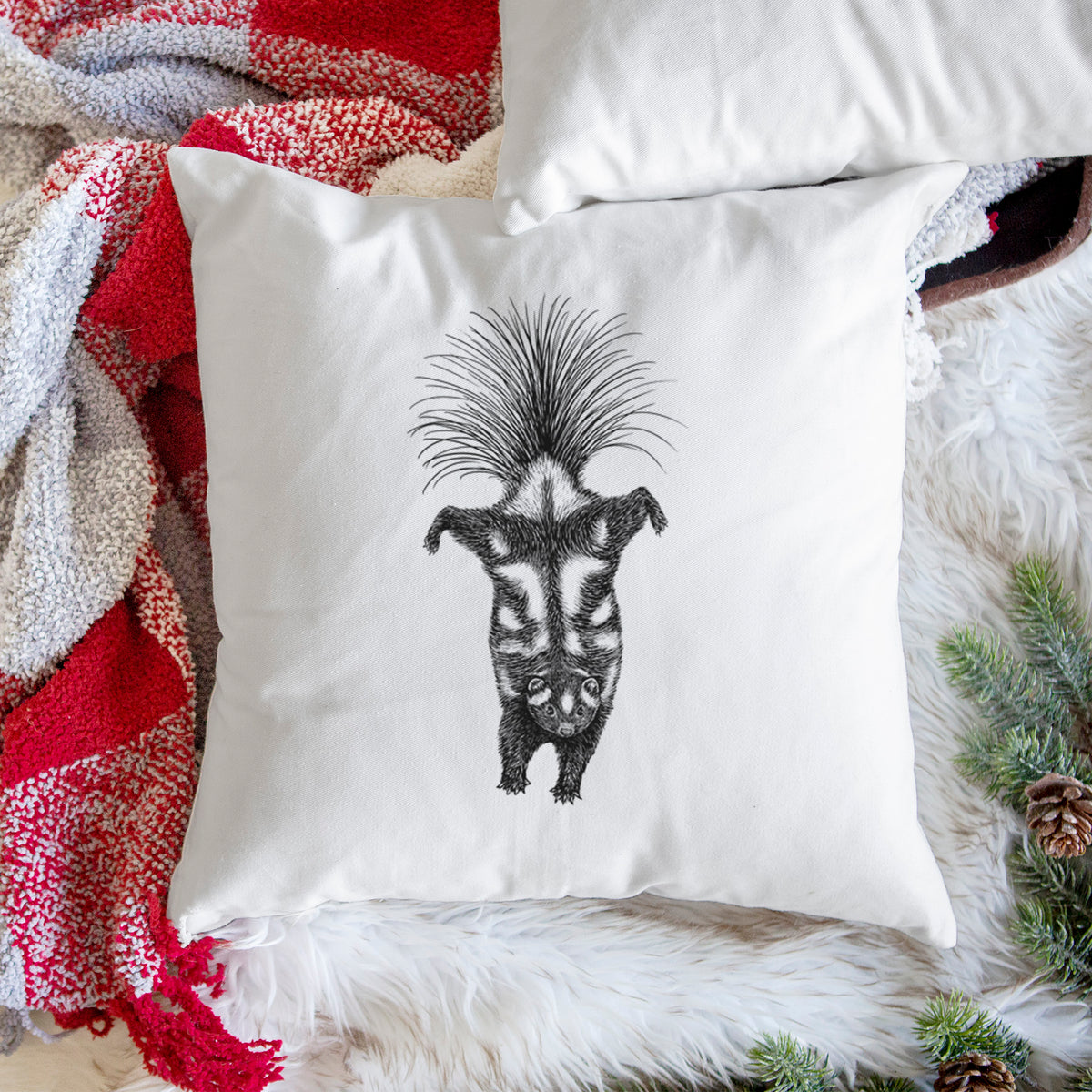 White pillow cover printed with a black ink illustration of a spotted skunk doing a handstand with its tail fanned, on a woven chair.