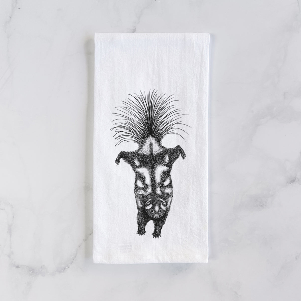 White cotton tea towel laid flat on marble, printed with a black ink illustration of a spotted skunk doing a handstand with its tail fanned.