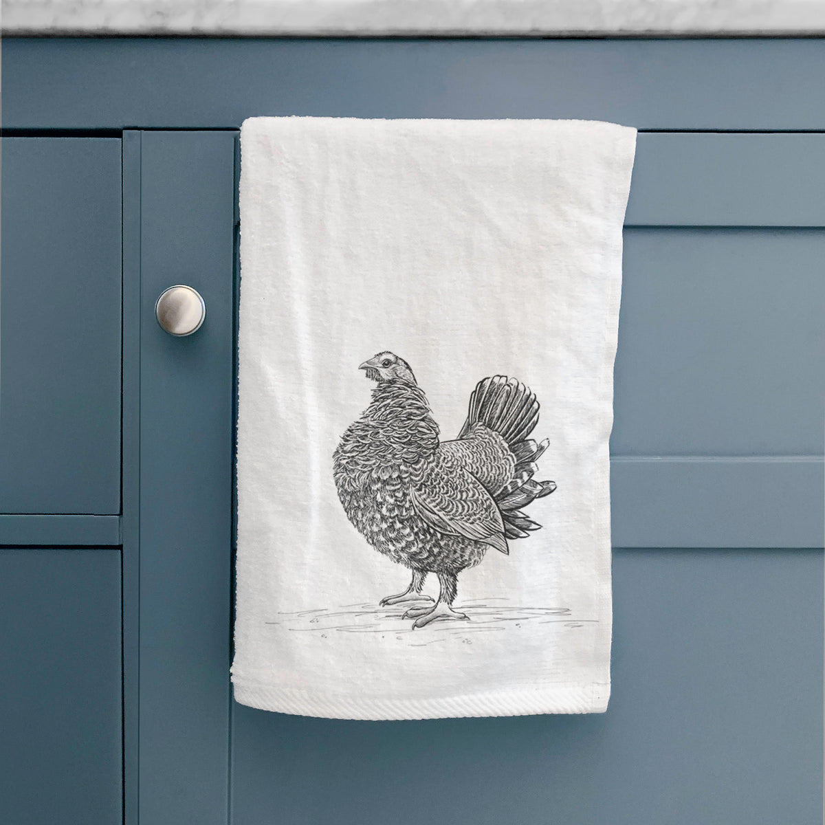 White hand towel printed with a detailed black ink illustration of a spruce grouse standing with its tail fanned, hanging on a cabinet door.