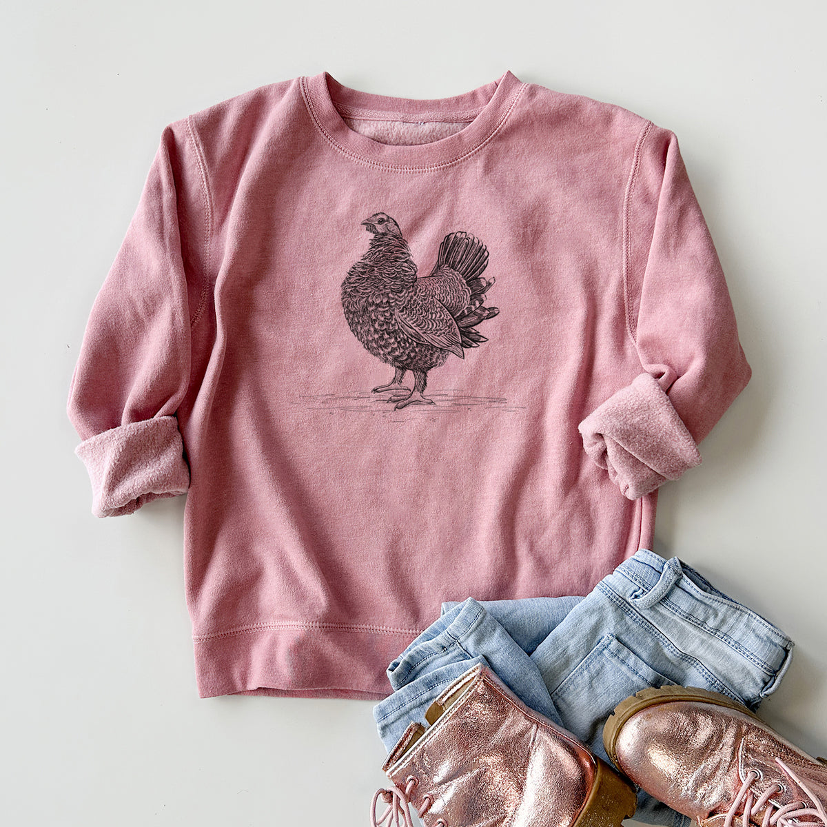 Youth crewneck sweatshirt printed with a detailed black ink illustration of a spruce grouse standing with its tail fanned, styled flat with jeans and boots.