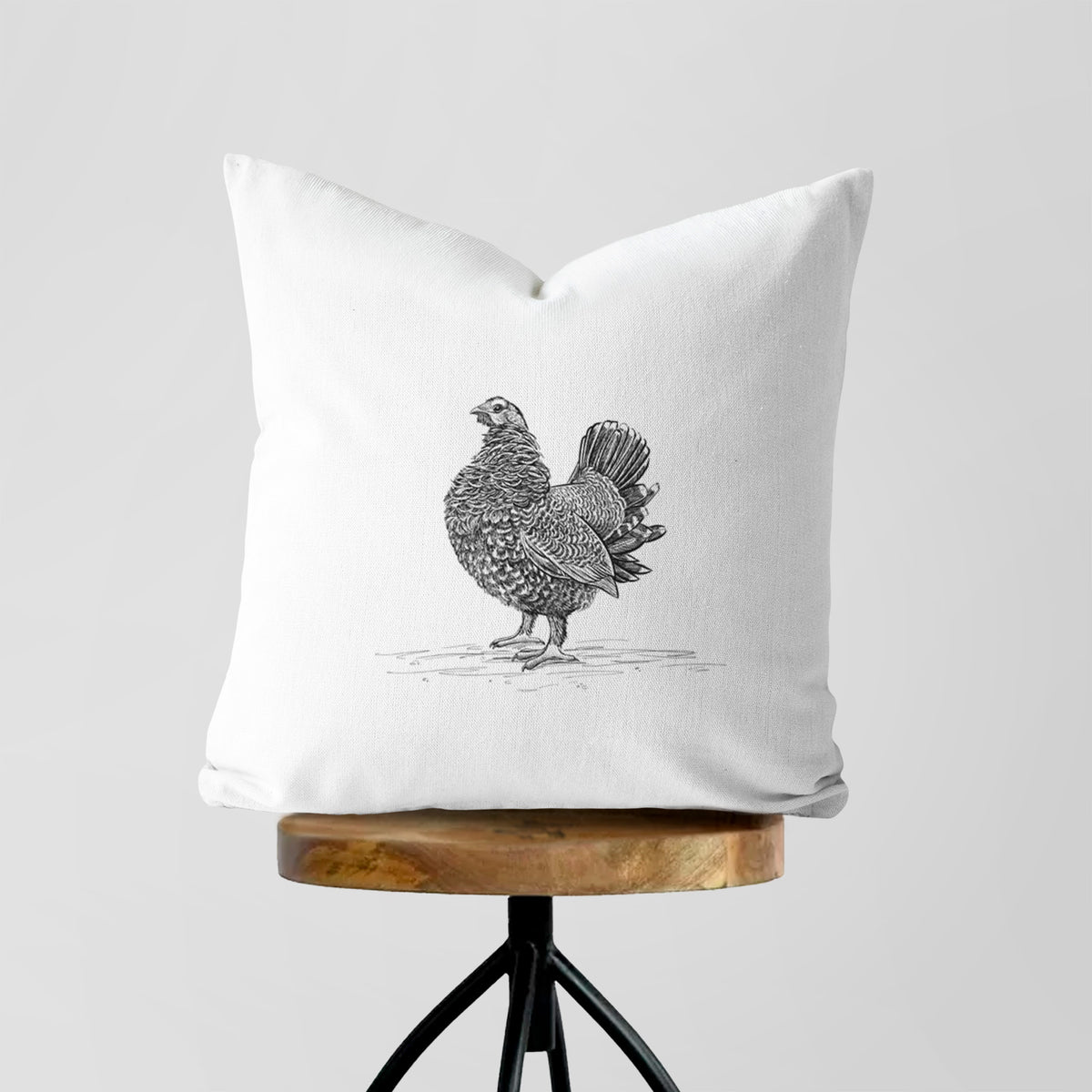 White pillow cover printed with a detailed black ink illustration of a spruce grouse standing with its tail fanned, on a wooden stool.
