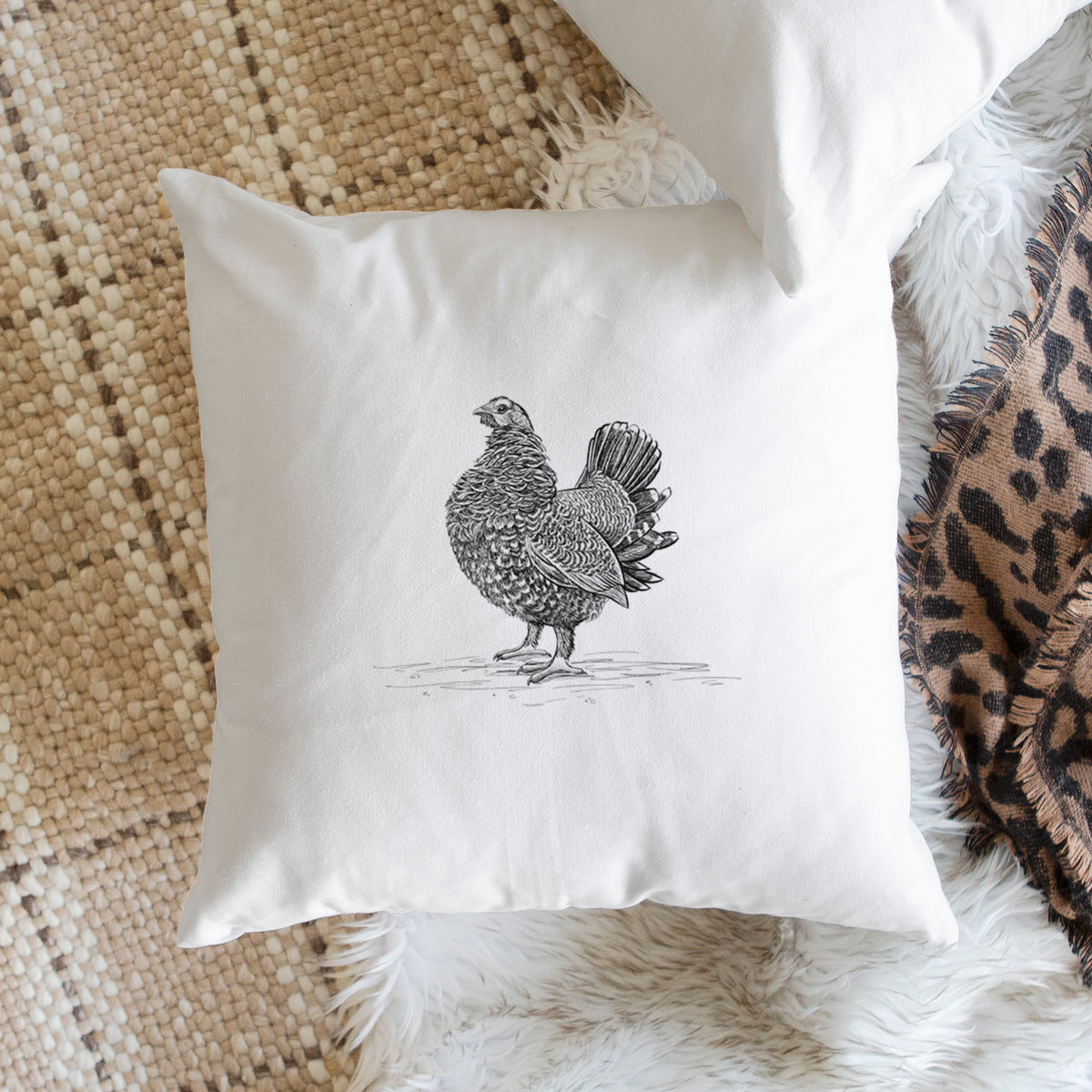 White pillow cover printed with a detailed black ink illustration of a spruce grouse standing with its tail fanned, on a woven chair.