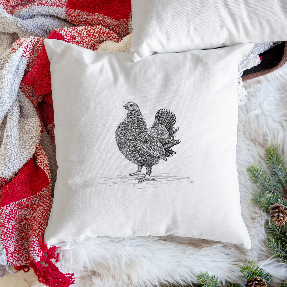 White pillow cover printed with a detailed black ink illustration of a spruce grouse standing with its tail fanned, on a woven chair.