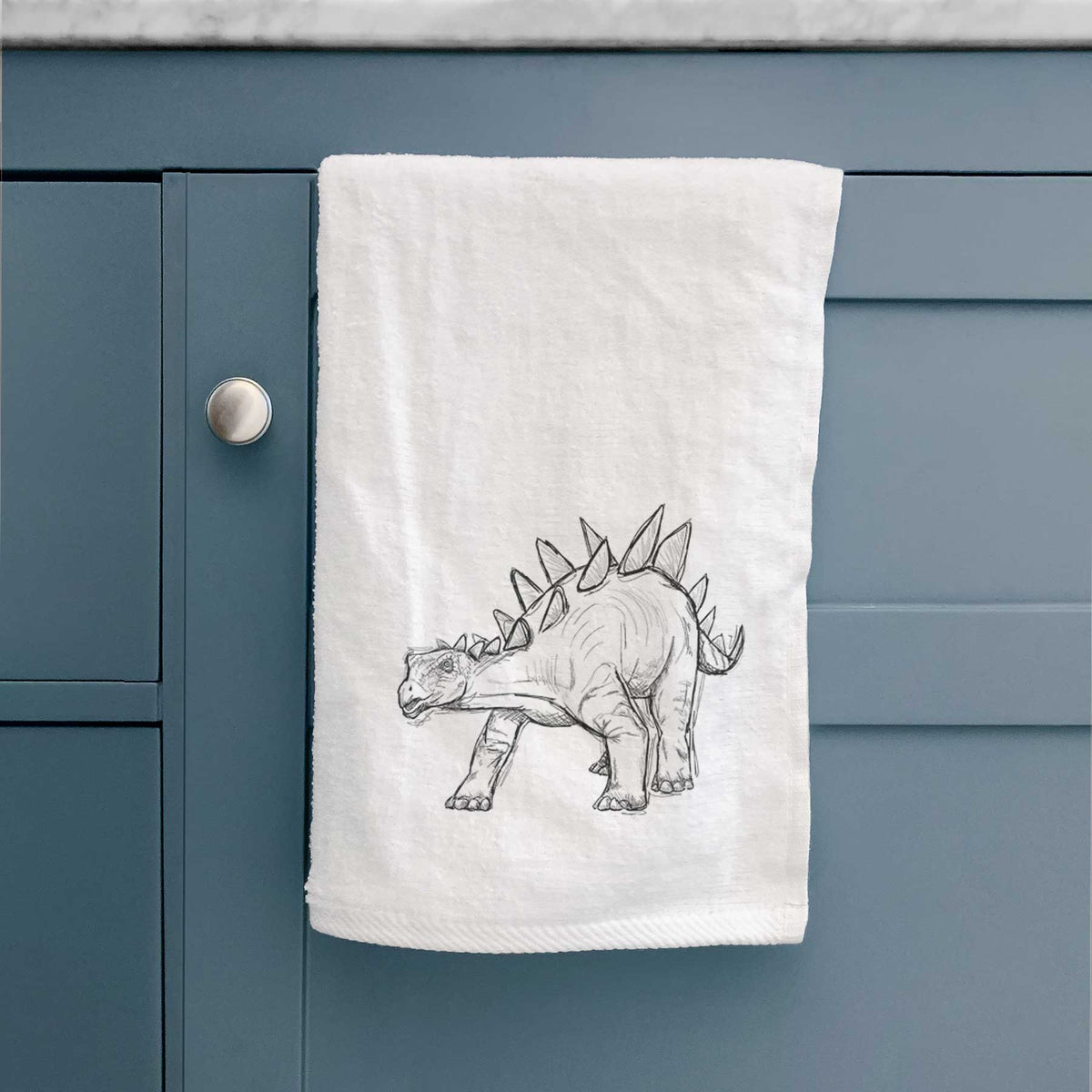 White hand towel printed with a black ink illustration of a Stegosaurus with plates along its back.