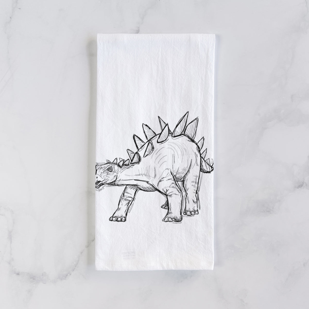 White cotton tea towel laid flat on marble, printed with a black ink illustration of a Stegosaurus with plates along its back.