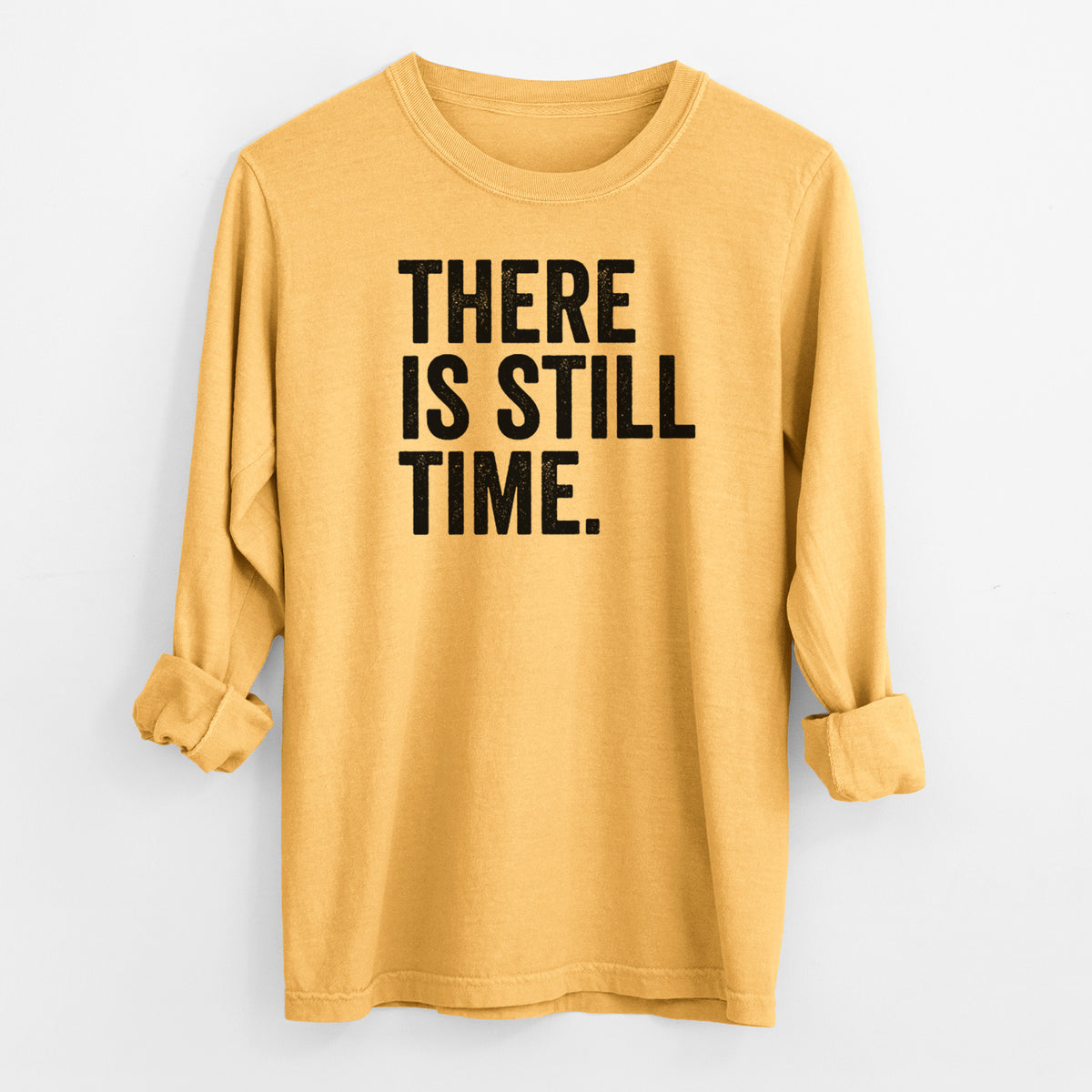 Golden wheat yellow Comfort Colors long sleeve shirt laid flat with the cuffs rolled, printed with bold black words reading There Is Still Time.